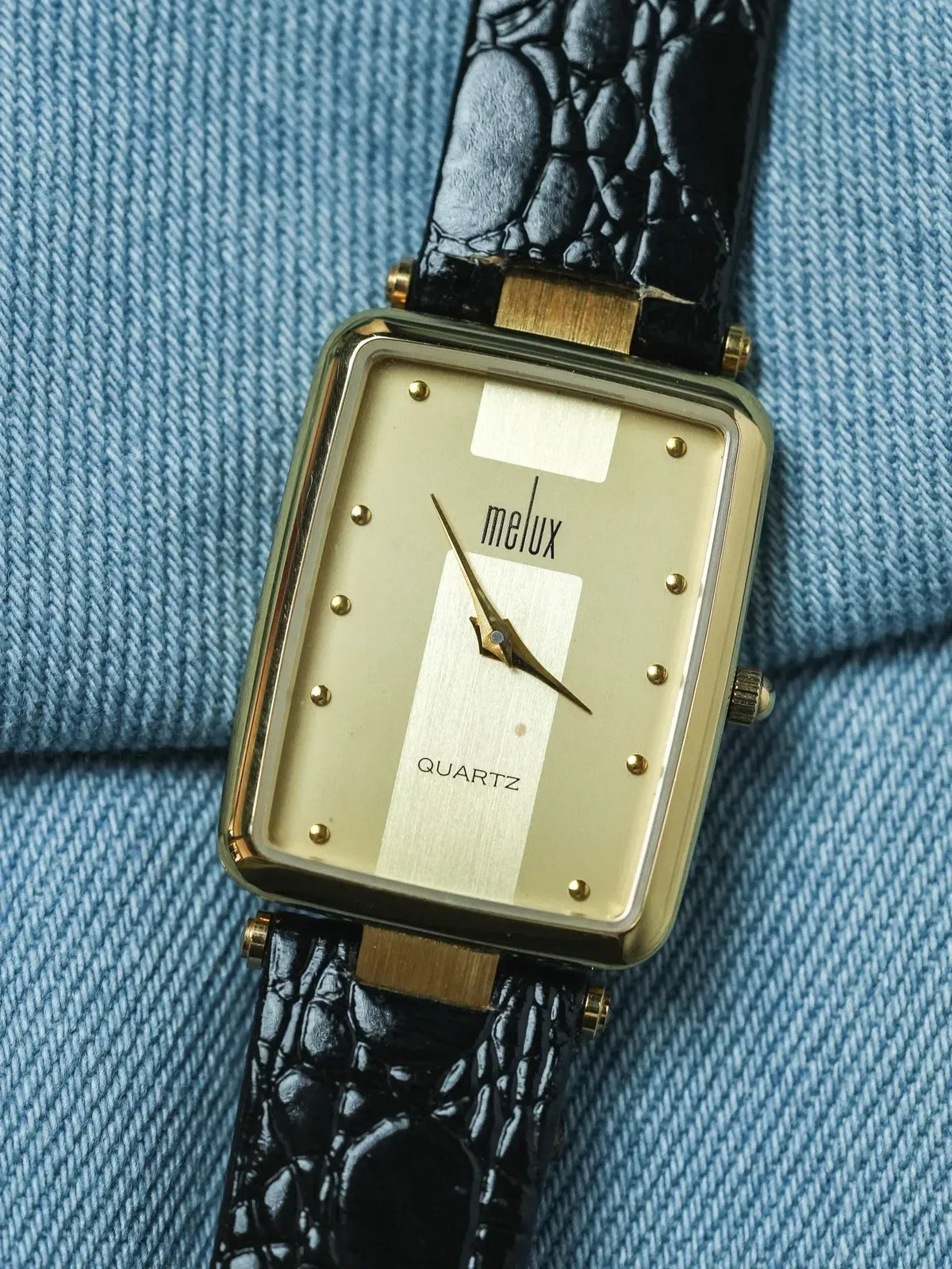 Melux vintage quartz watch with gold case, cream dial, and black croco strap on denim