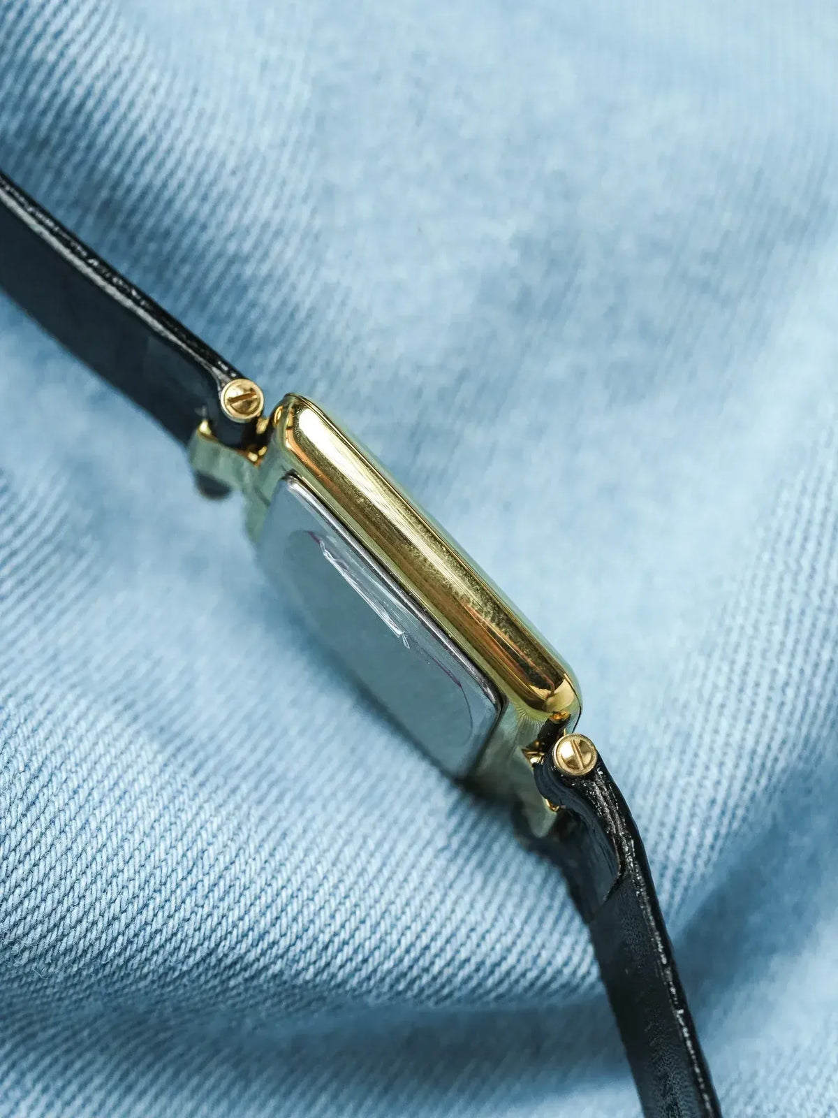 Vintage Cartier watch with gold case and black leather strap on denim