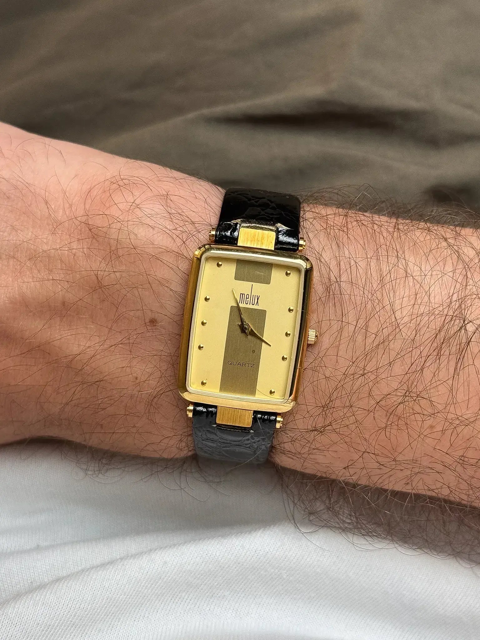 Melux vintage quartz watch with gold case, black leather strap, worn on wrist