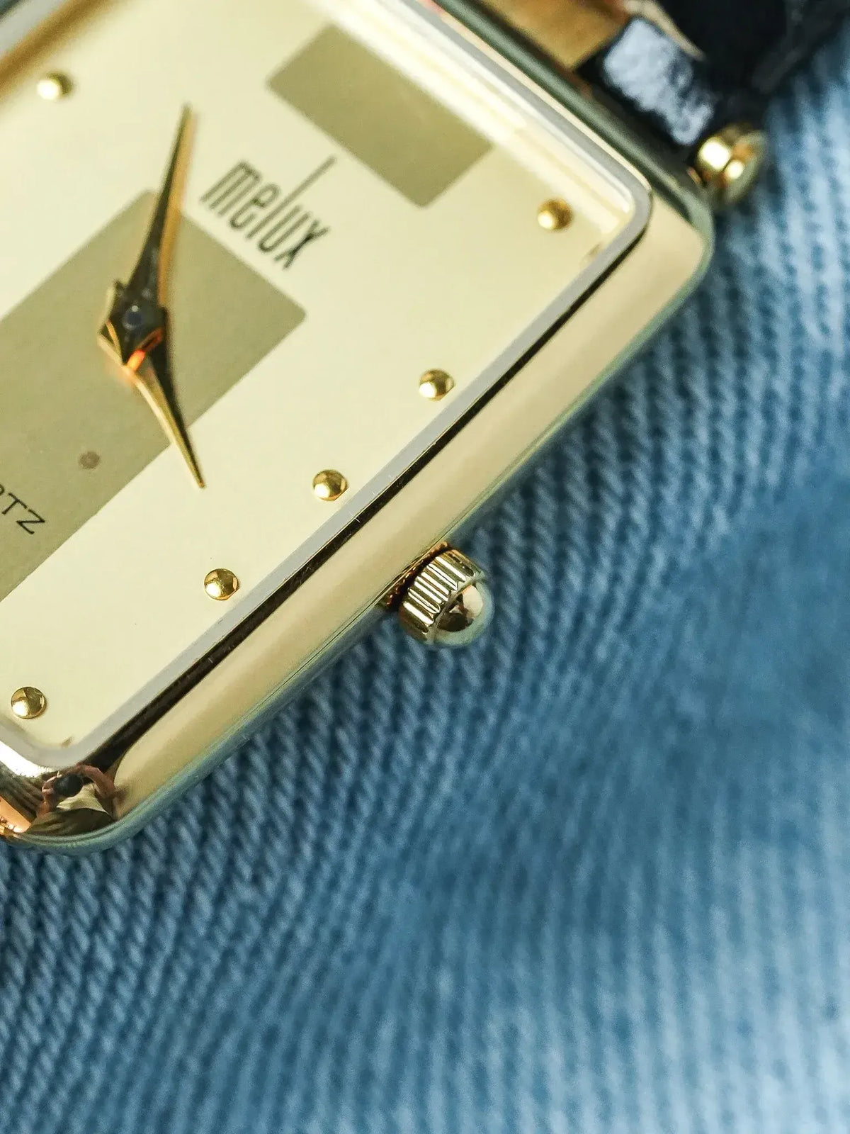 Melux vintage watch with gold case, cream dial, and black leather strap on denim