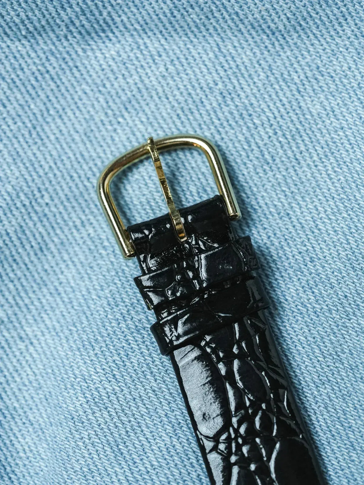 Black alligator leather watch strap with gold buckle on denim background