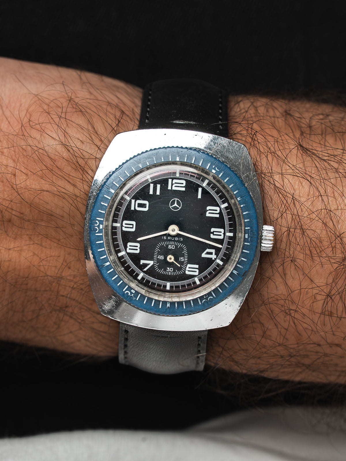 Montre Mercedes vintage, boîtier acier, cadran noir et lunette bleue, portée au poignet