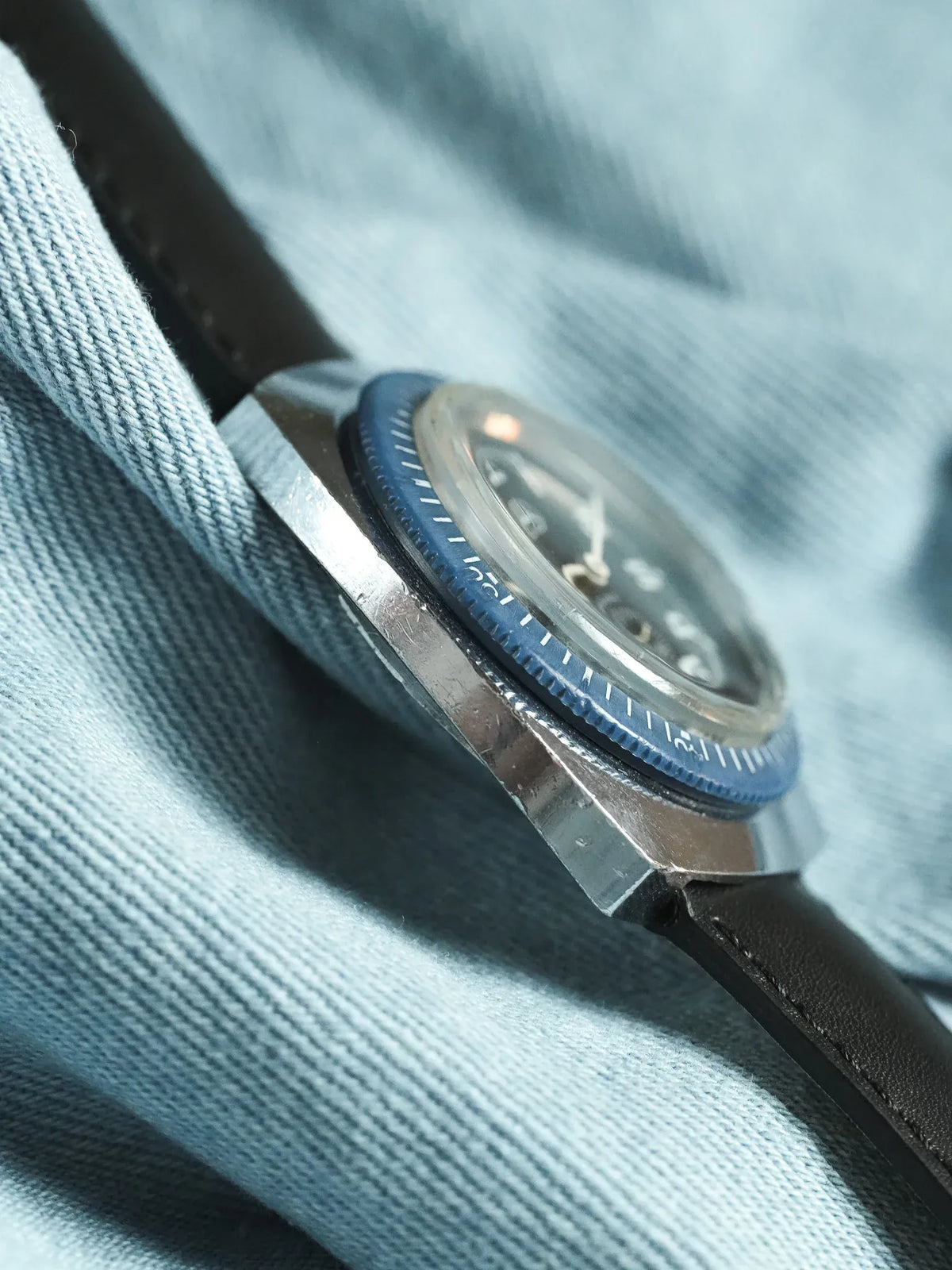 Vintage Omega Seamaster with blue bezel, steel case, black dial, leather strap on denim
