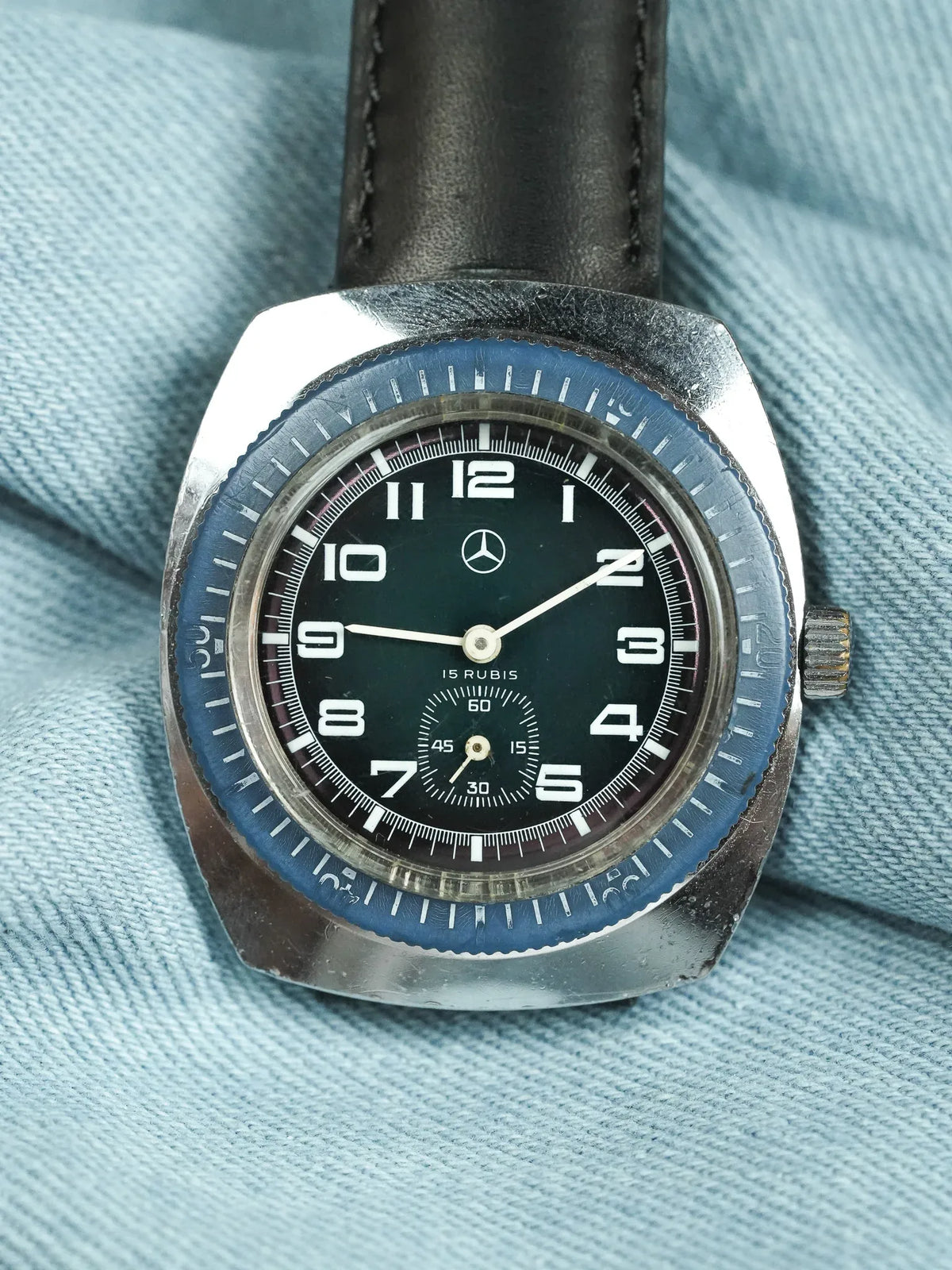 Vintage Mercedes-Benz watch with black dial, blue bezel, and leather strap on denim