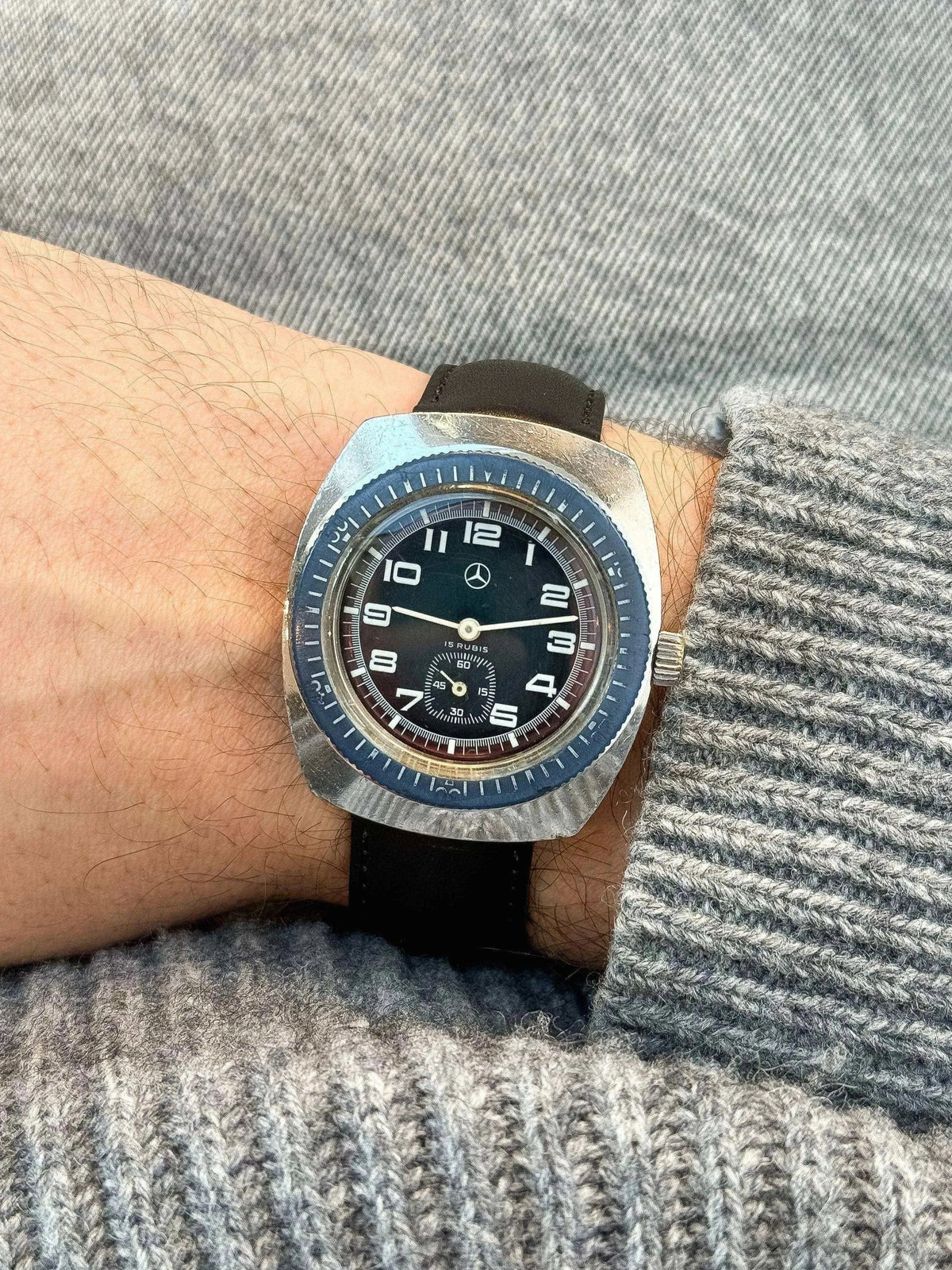 Vintage Mercedes-Benz watch with black dial, blue bezel, and leather strap on wrist