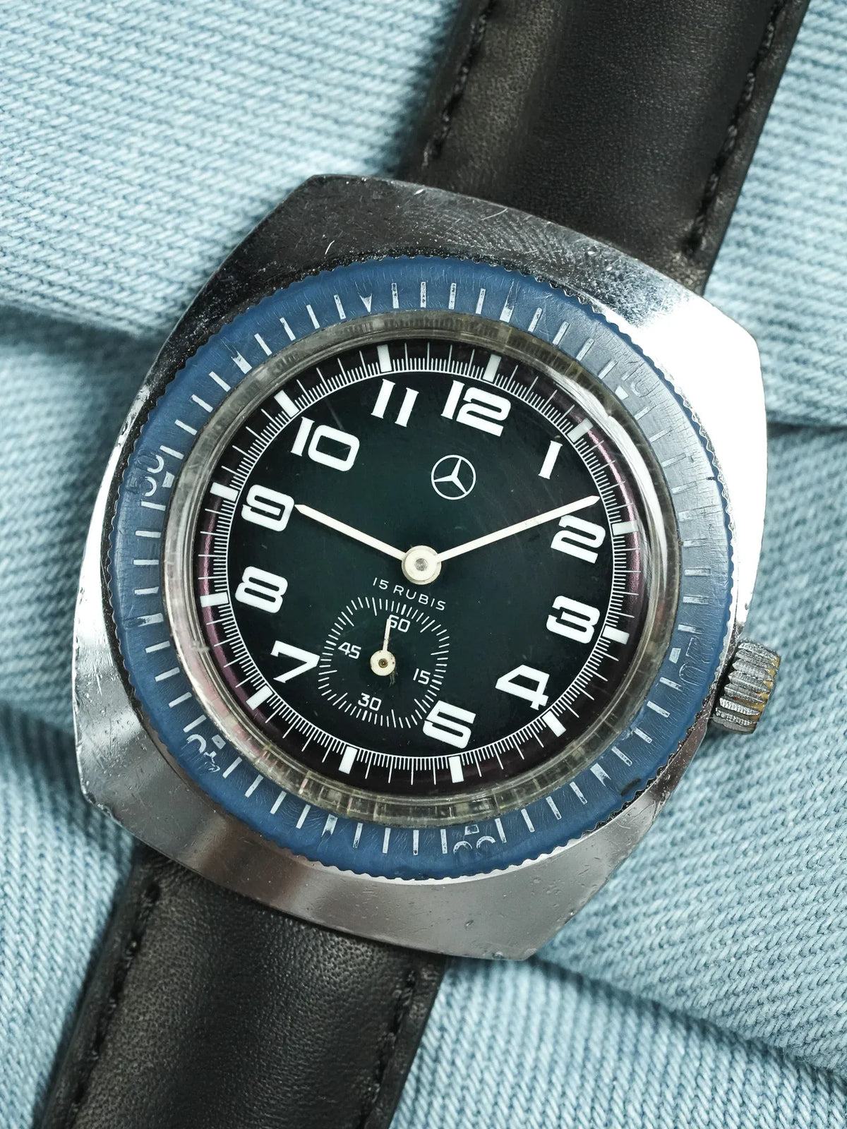 Vintage Mercedes-Benz watch with black dial, blue bezel, and black leather strap on denim