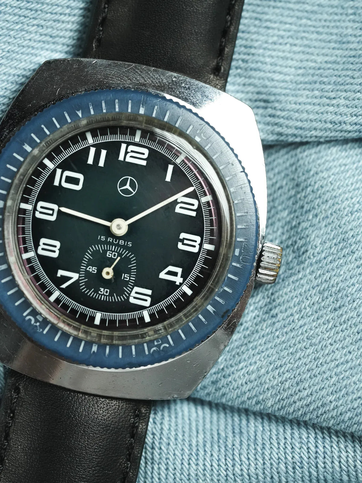 Vintage Mercedes-Benz watch with black dial, blue bezel, and black leather strap on denim
