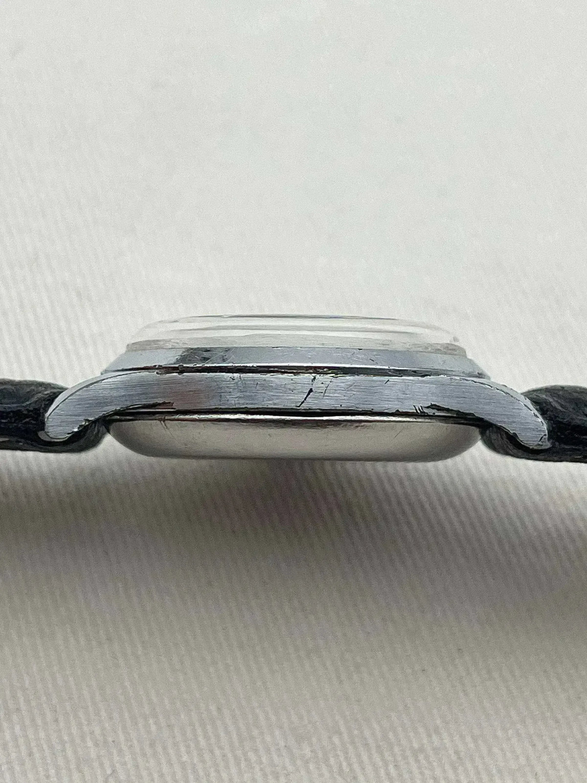 Vintage Omega watch side profile, stainless steel case, black leather strap, on white fabric