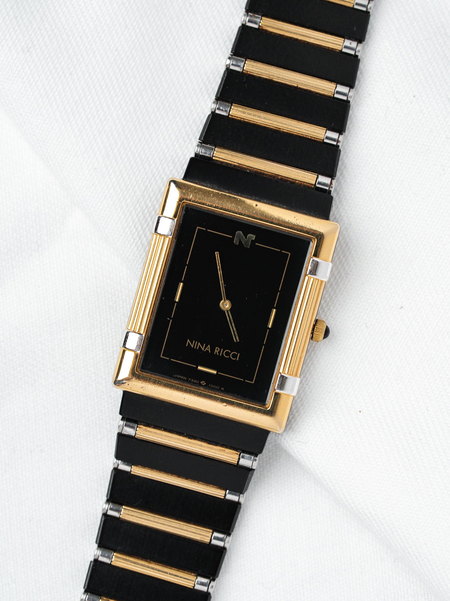Nina Ricci vintage watch with black dial, gold accents, and two-tone bracelet on white background