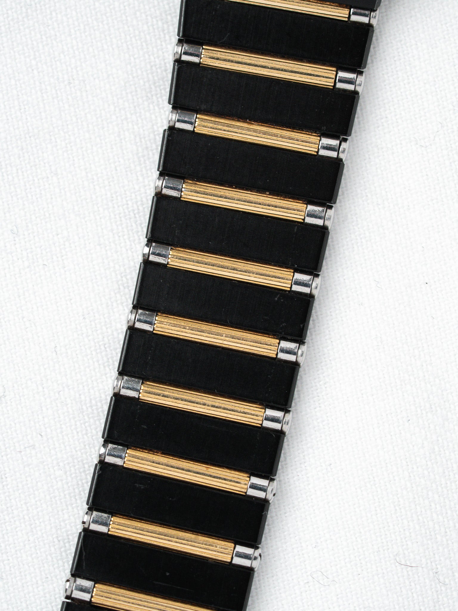 Vintage watch bracelet with black and gold-toned links on white background