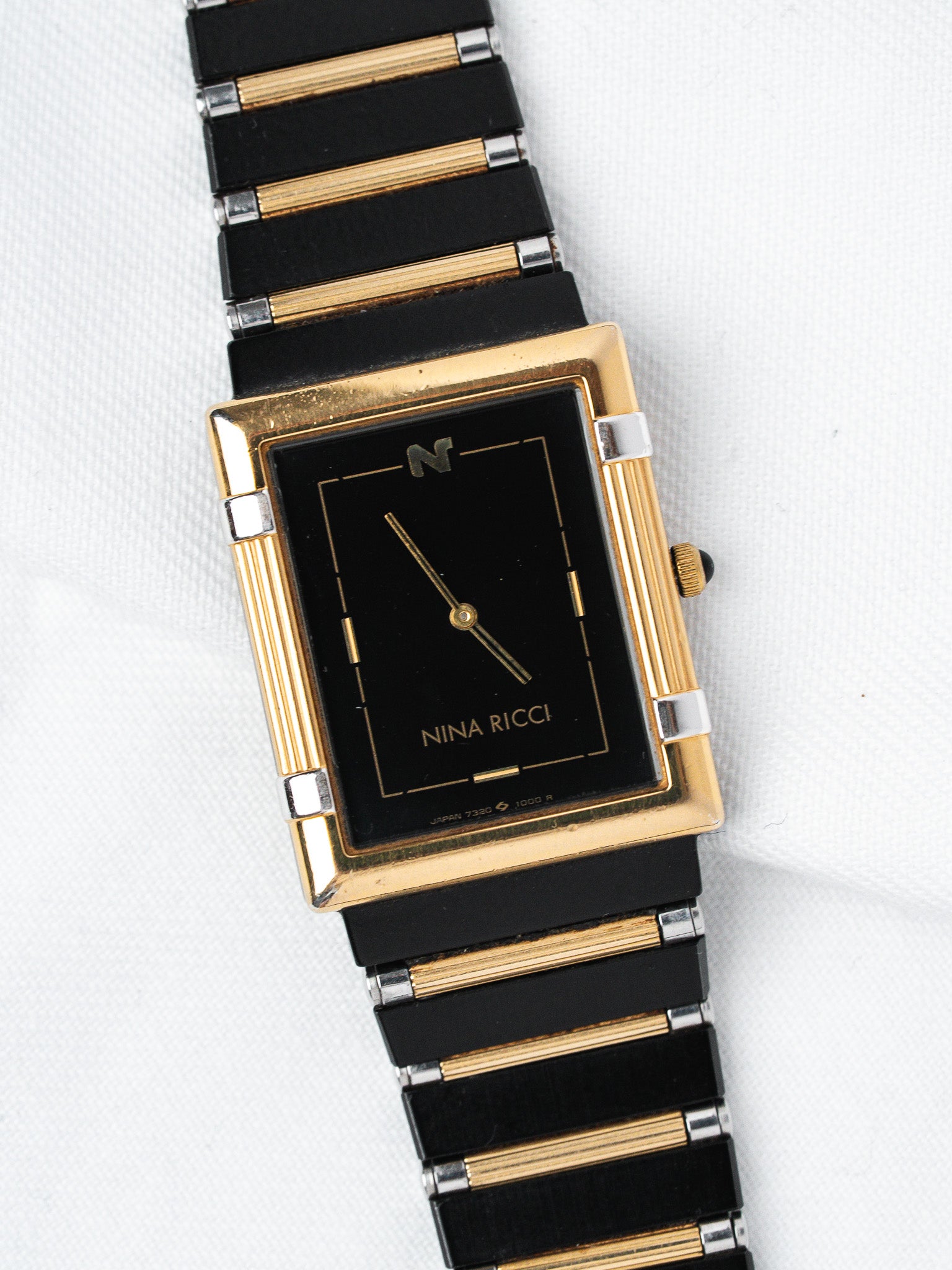 Nina Ricci vintage watch with black dial, gold case, and two-tone bracelet on white background