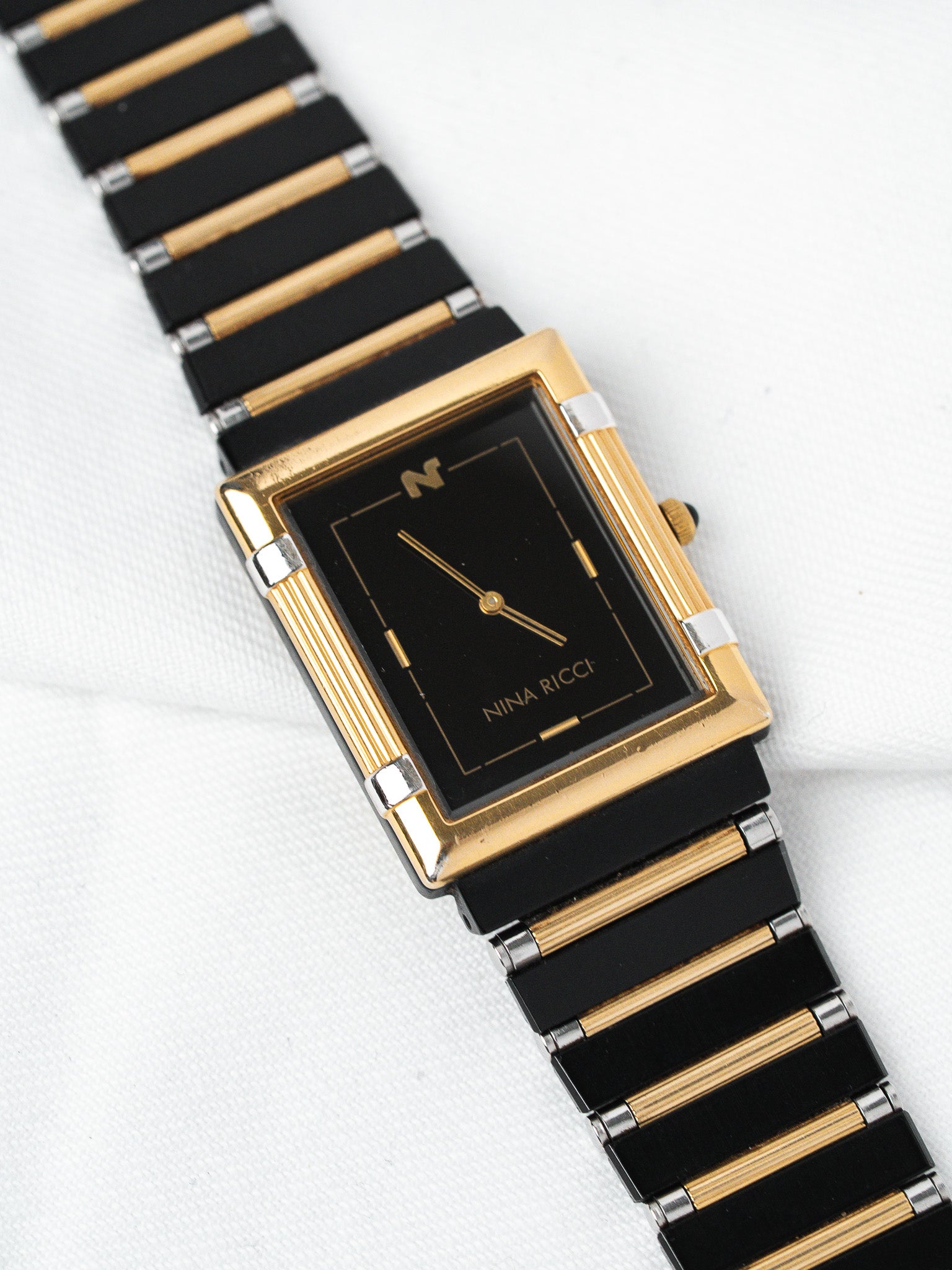 Nina Ricci vintage watch with black dial, gold accents, and two-tone bracelet on white background