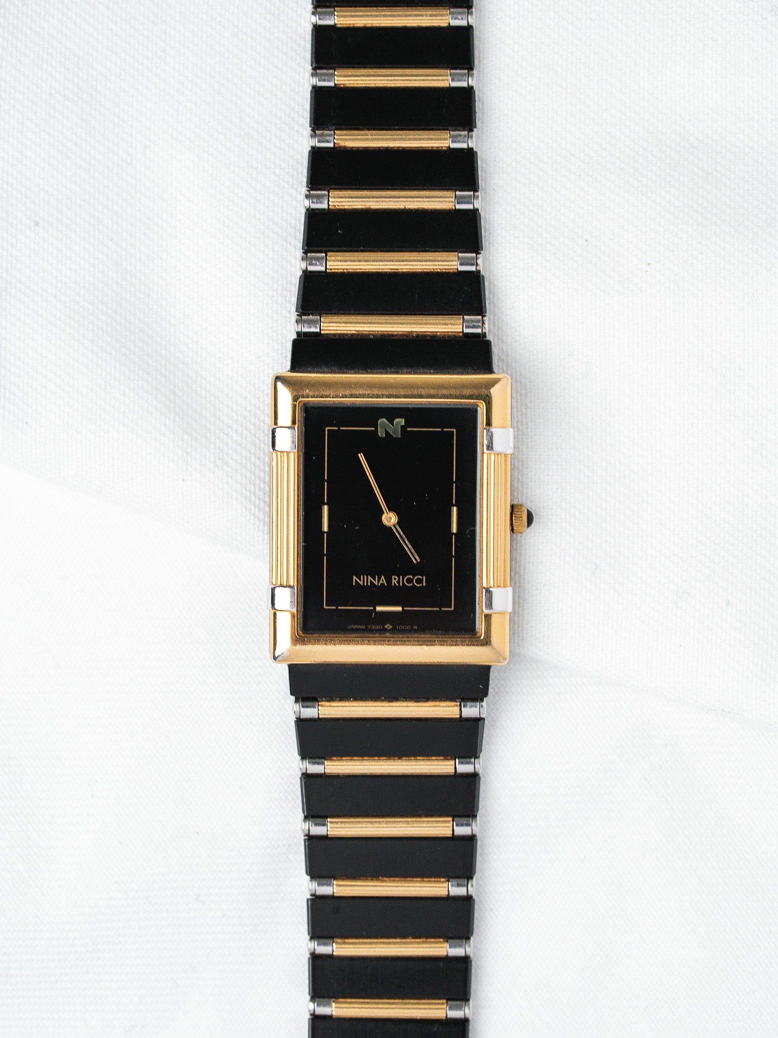 Nina Ricci vintage watch with black dial, gold case, and two-tone bracelet on white background