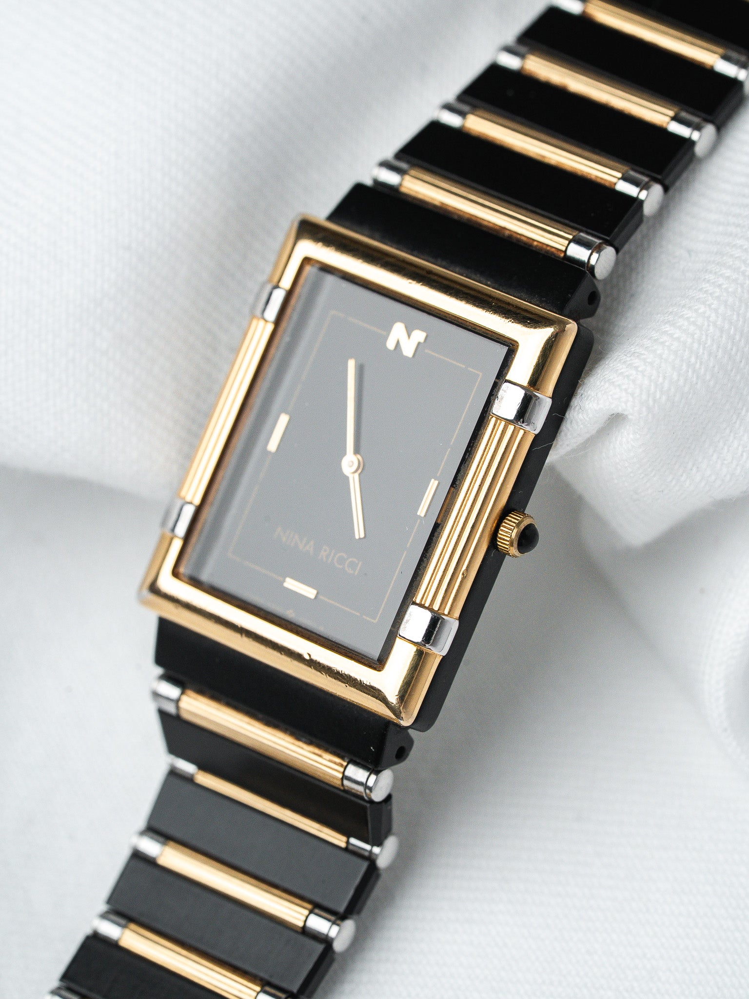 Nina Ricci vintage watch with black and gold bracelet, grey dial on white fabric