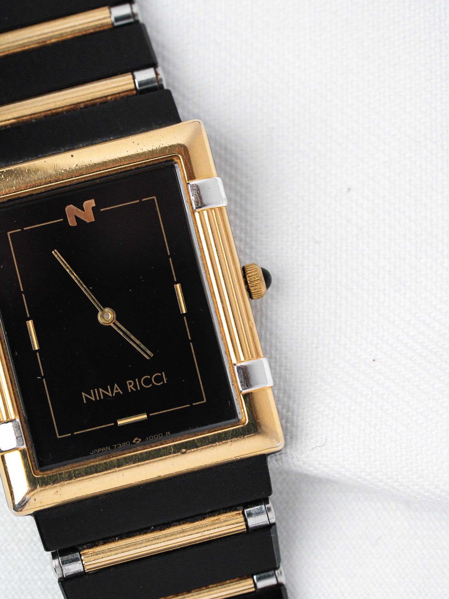 Nina Ricci vintage watch with black dial, gold accents, and black bracelet on white background