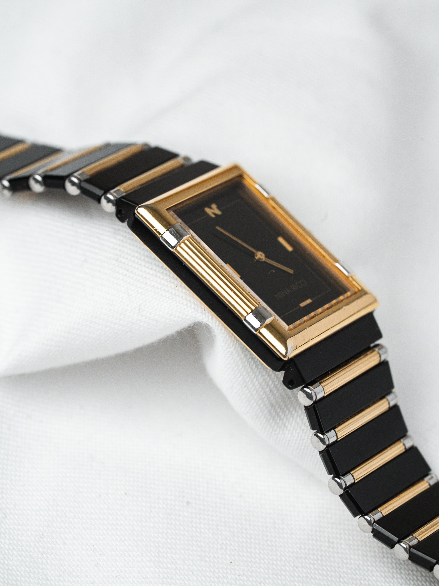 Nina Ricci vintage watch with black dial, gold case, and black-gold bracelet on white fabric