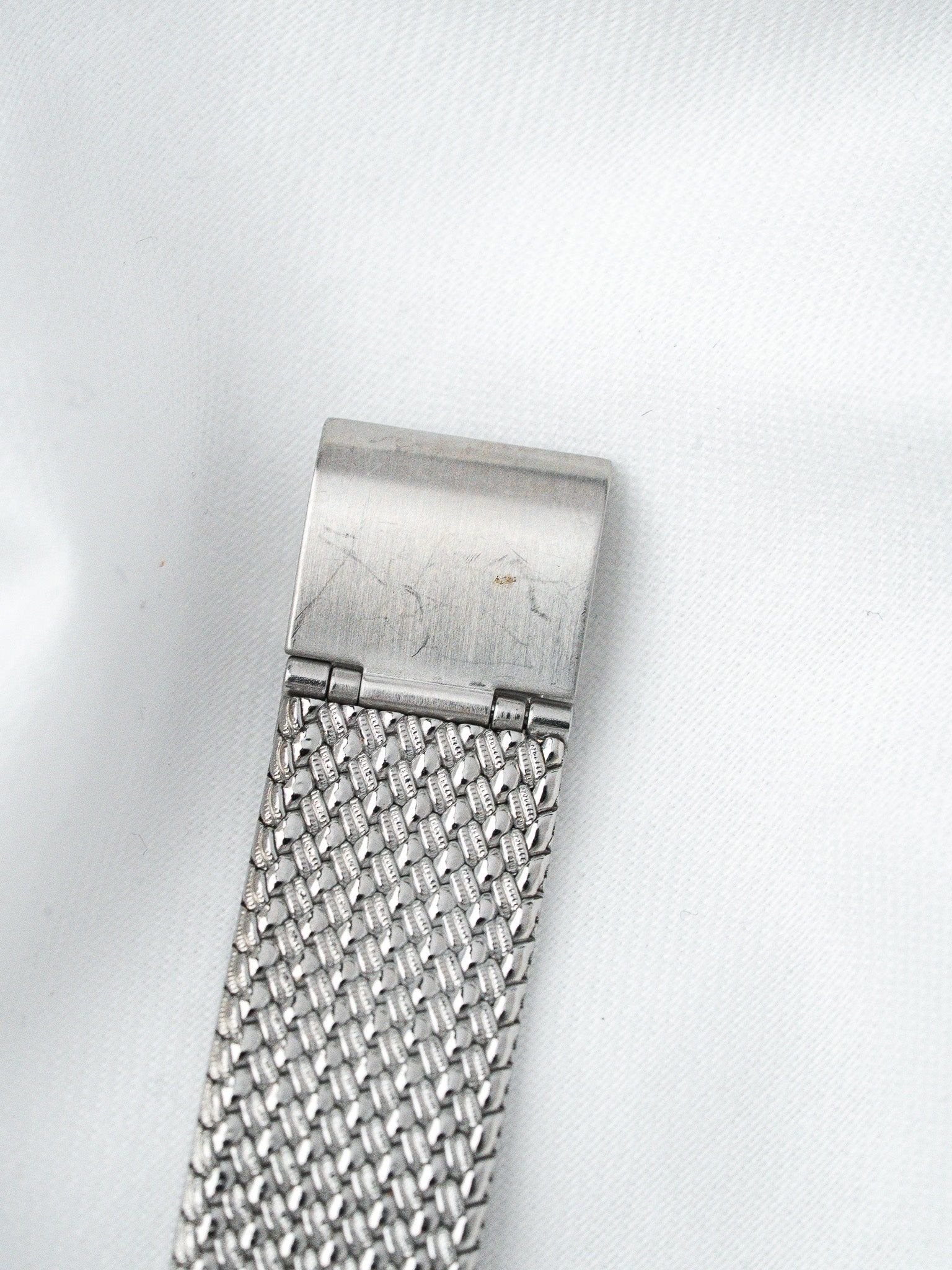 Vintage stainless steel mesh watch bracelet with textured clasp on white background
