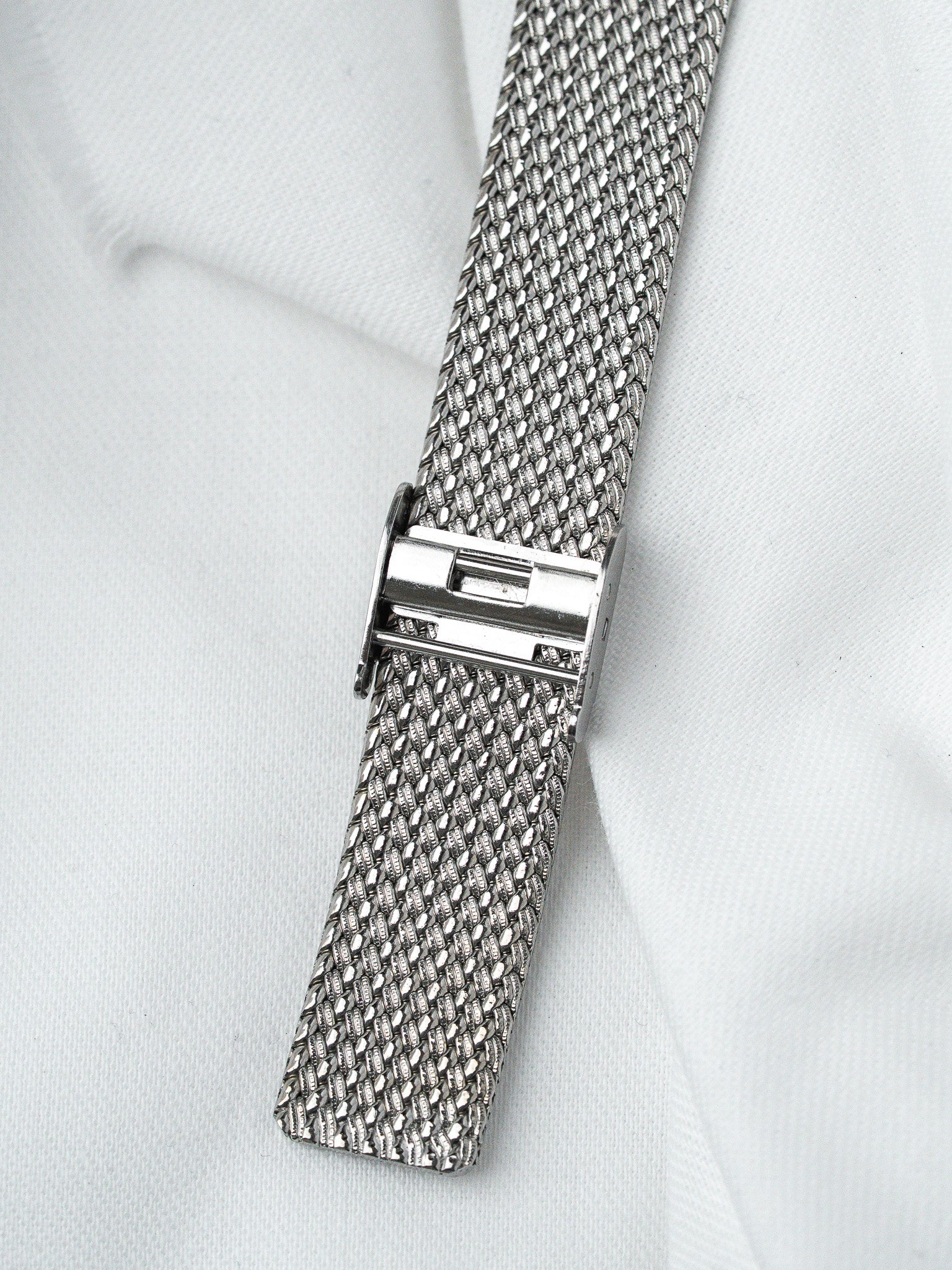 Vintage steel mesh watch strap with secure clasp on white fabric