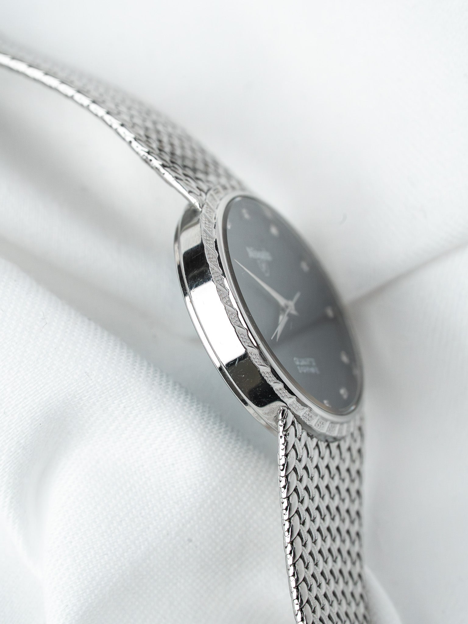 Vintage Seiko watch with dark dial, textured bezel, and mesh bracelet on white fabric