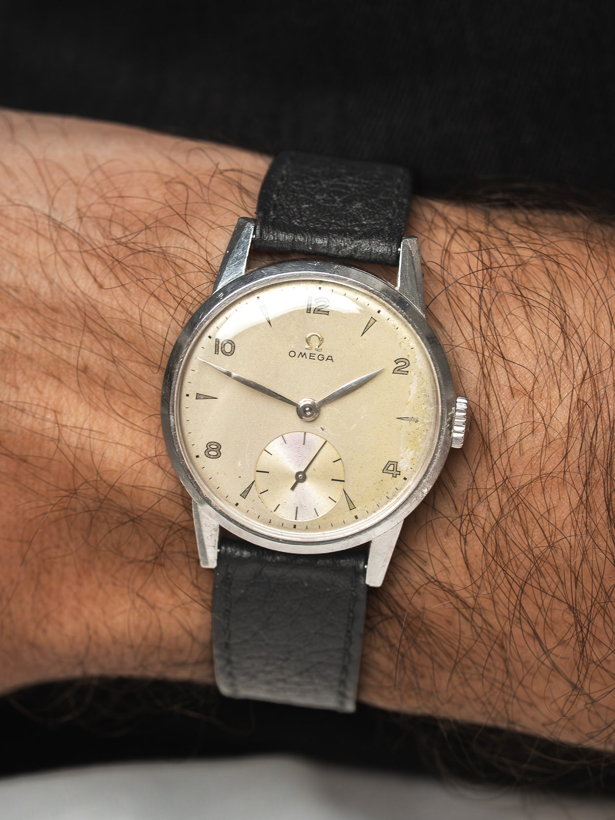 Montre Omega vintage avec cadran champagne et bracelet en cuir noir au poignet.