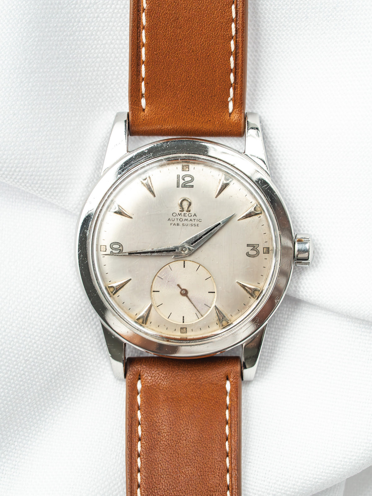 Omega vintage automatic watch with silver dial, brown leather strap, on white fabric