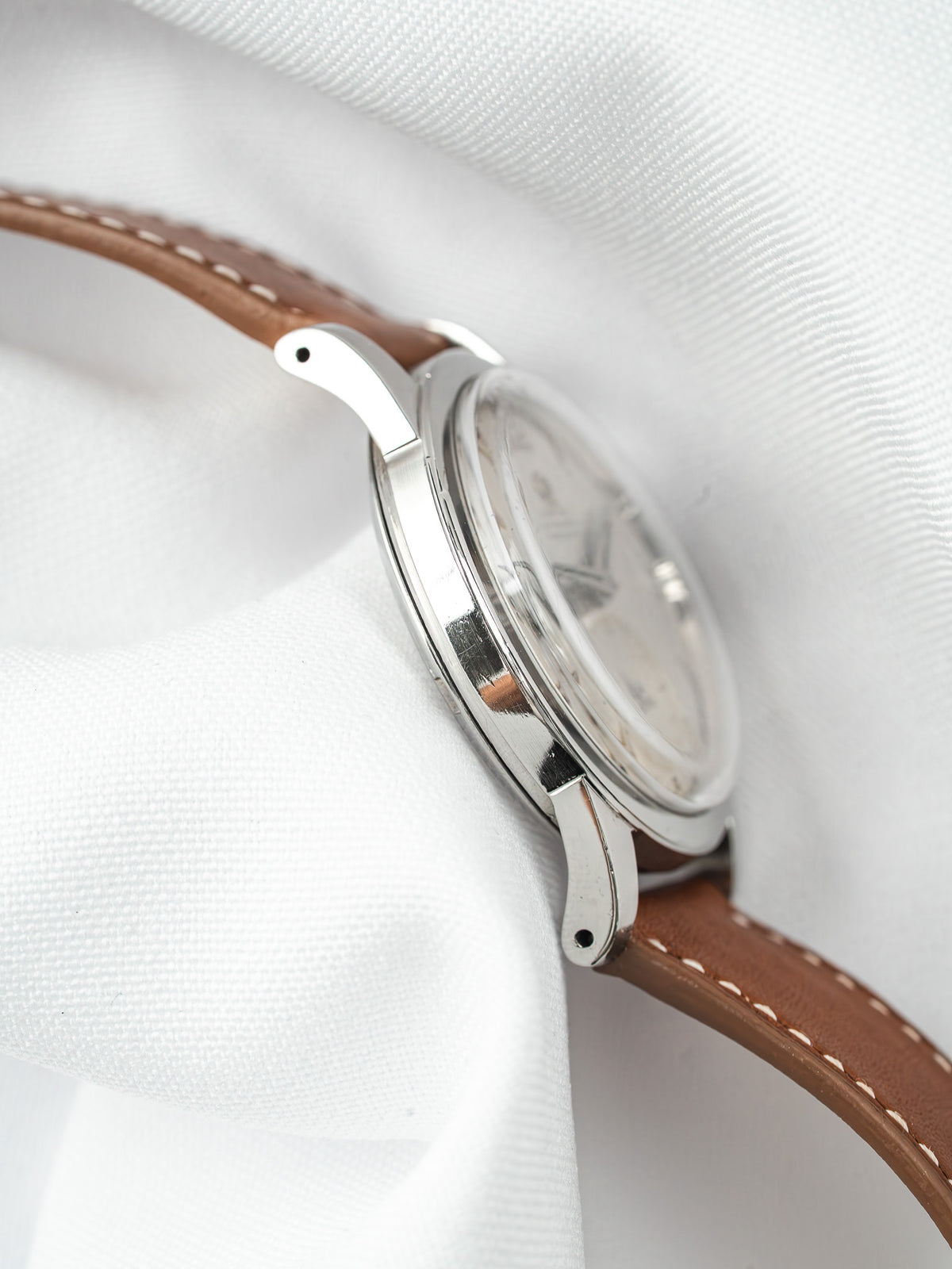 Vintage Omega watch with silver case, brown leather strap, on white fabric