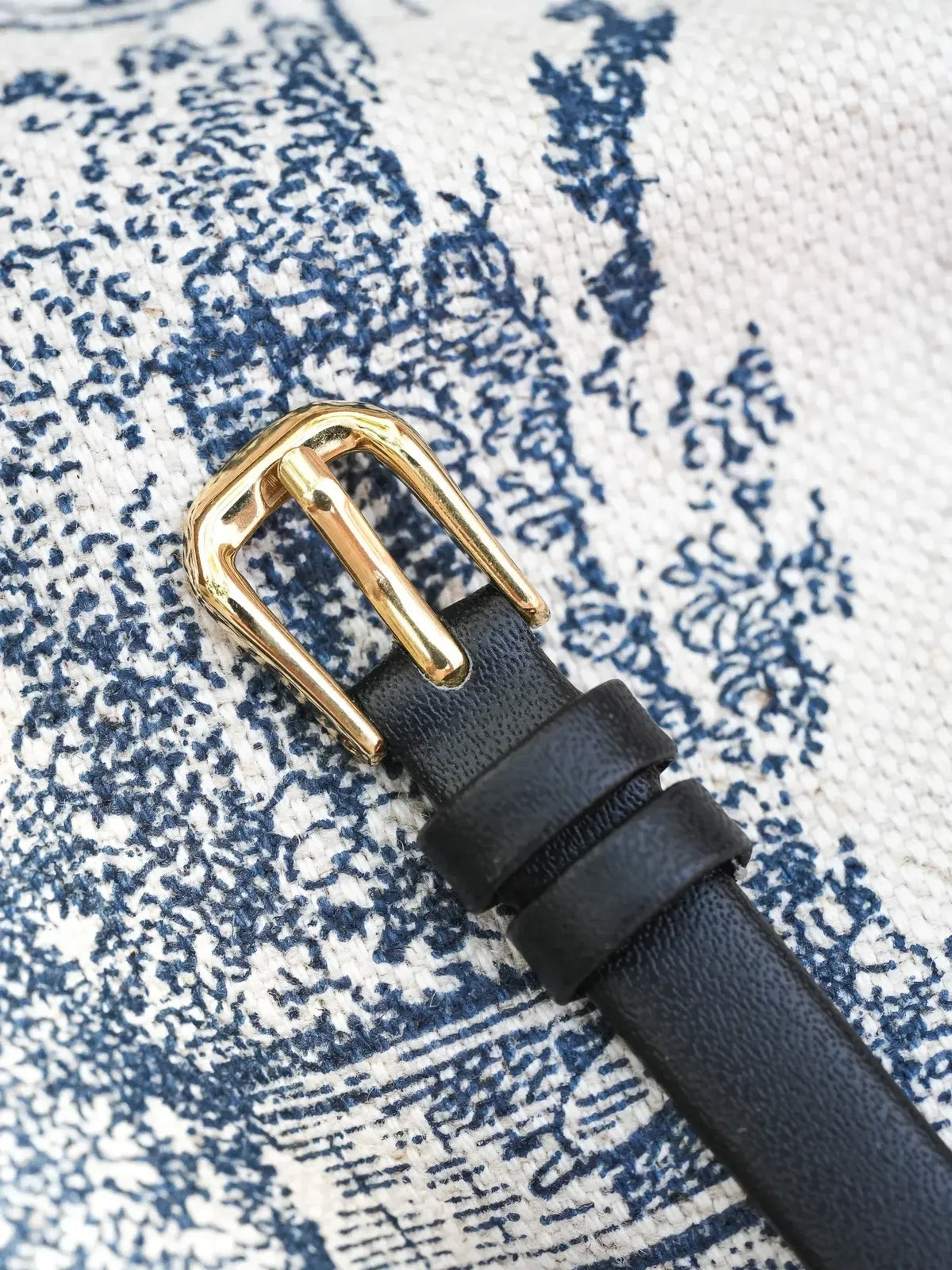 Black leather belt with gold-tone buckle on patterned fabric background