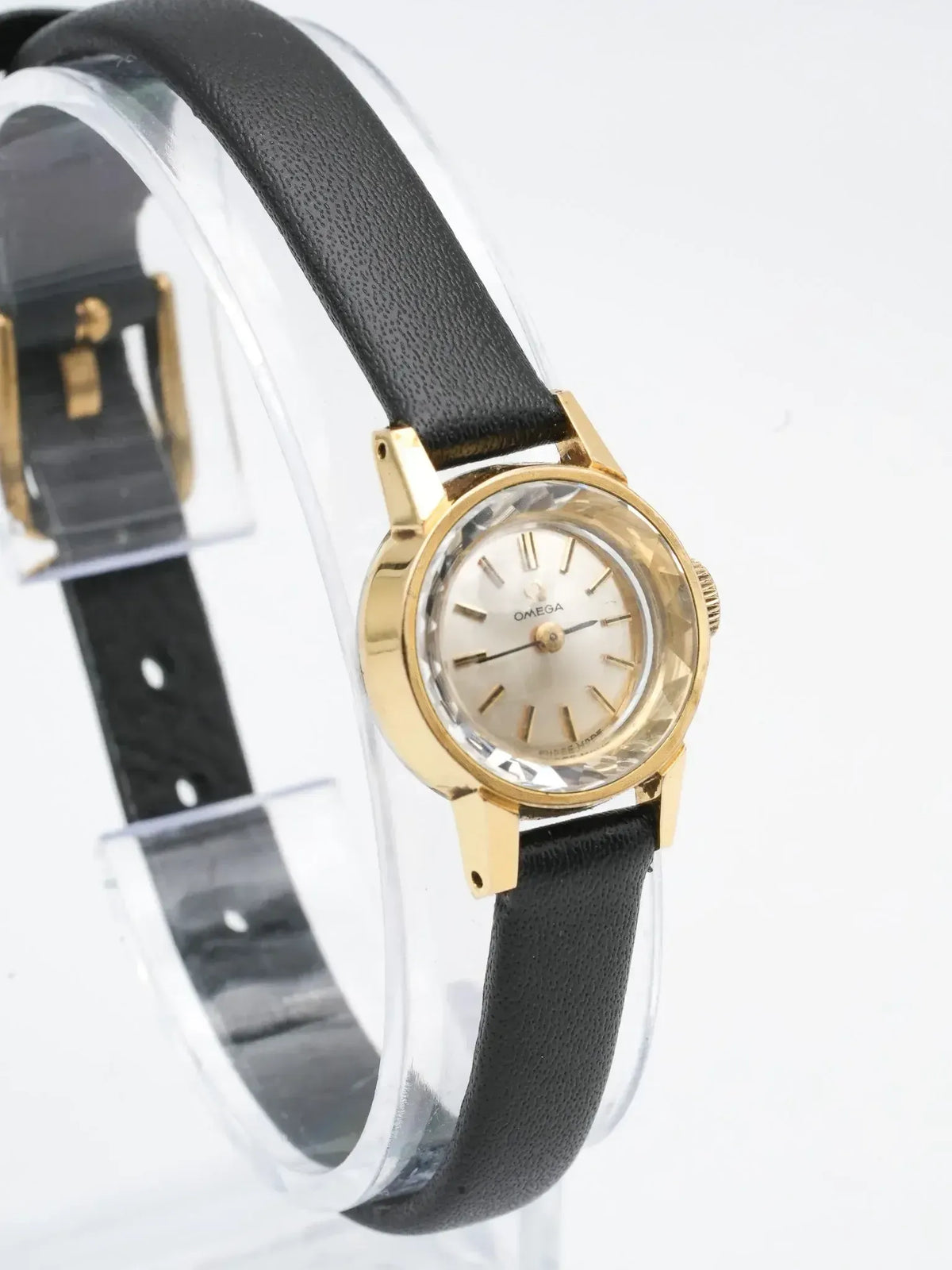 Vintage Omega watch with gold case, silver dial, and black leather strap on display stand