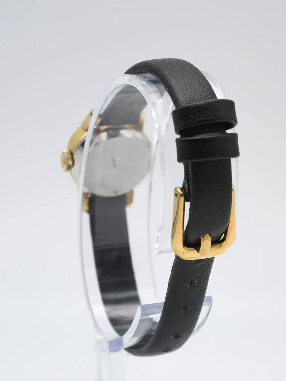 Vintage watch with gold case, black leather strap, and gold buckle on display stand