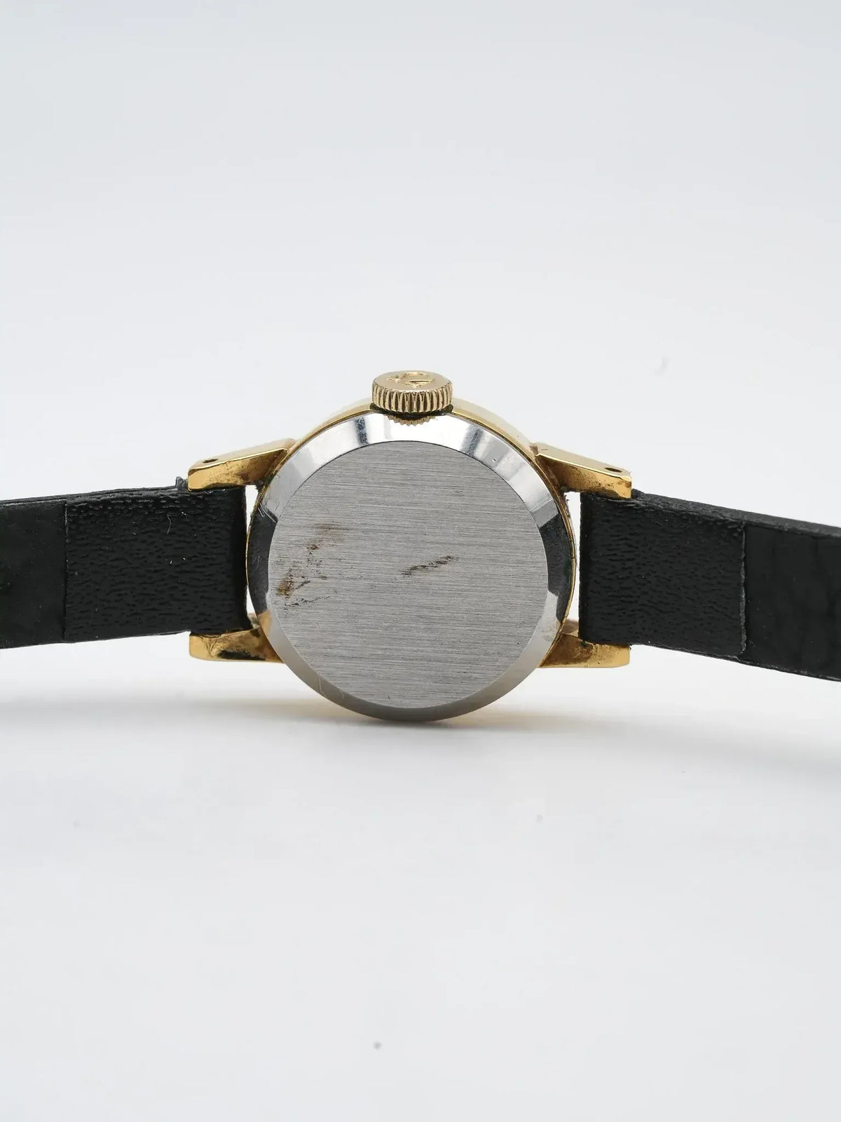 Vintage watch with gold case, black leather strap, and brushed steel back on white background