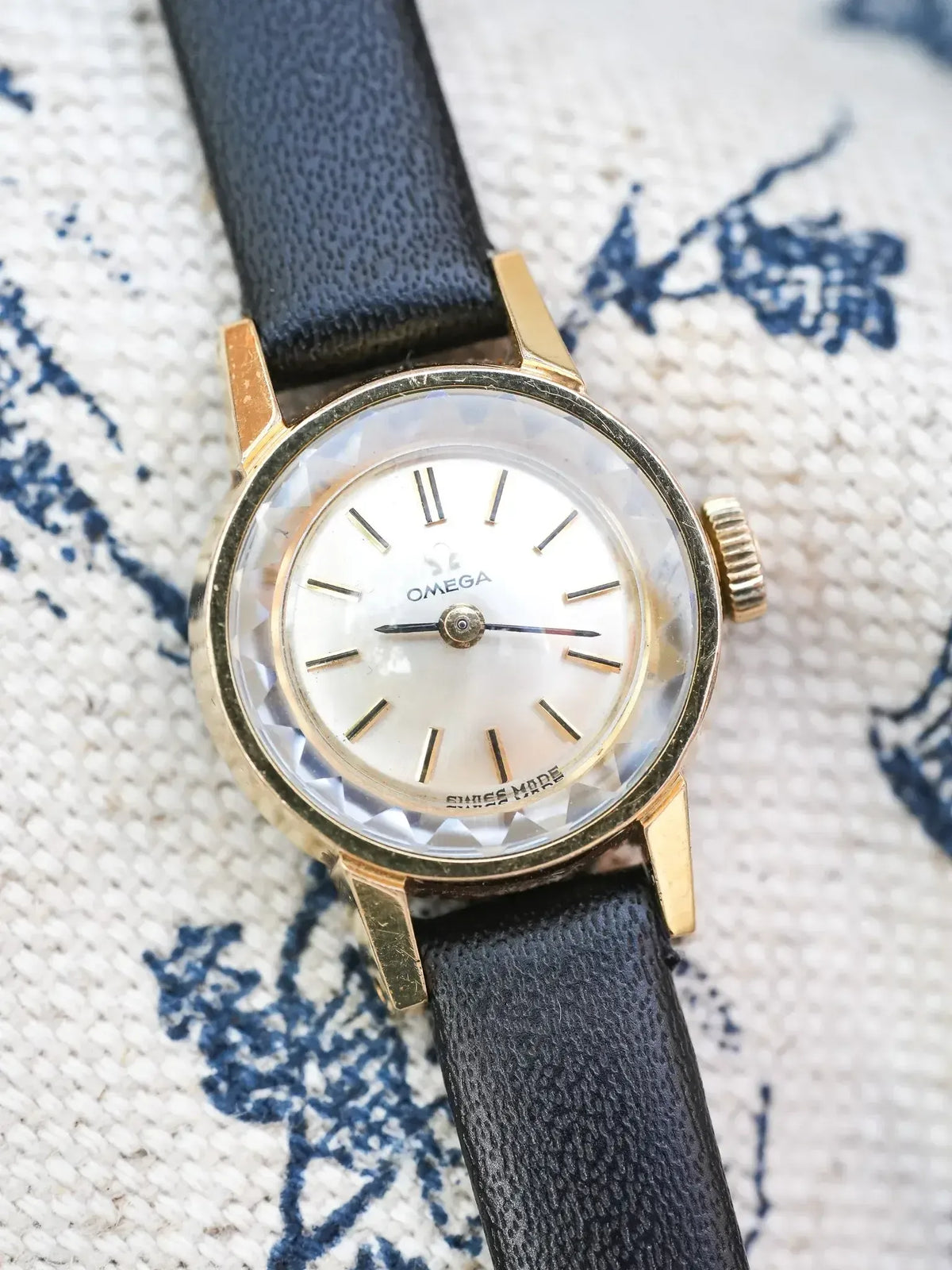Vintage Omega watch with gold case, mother-of-pearl dial, black leather strap on patterned fabric