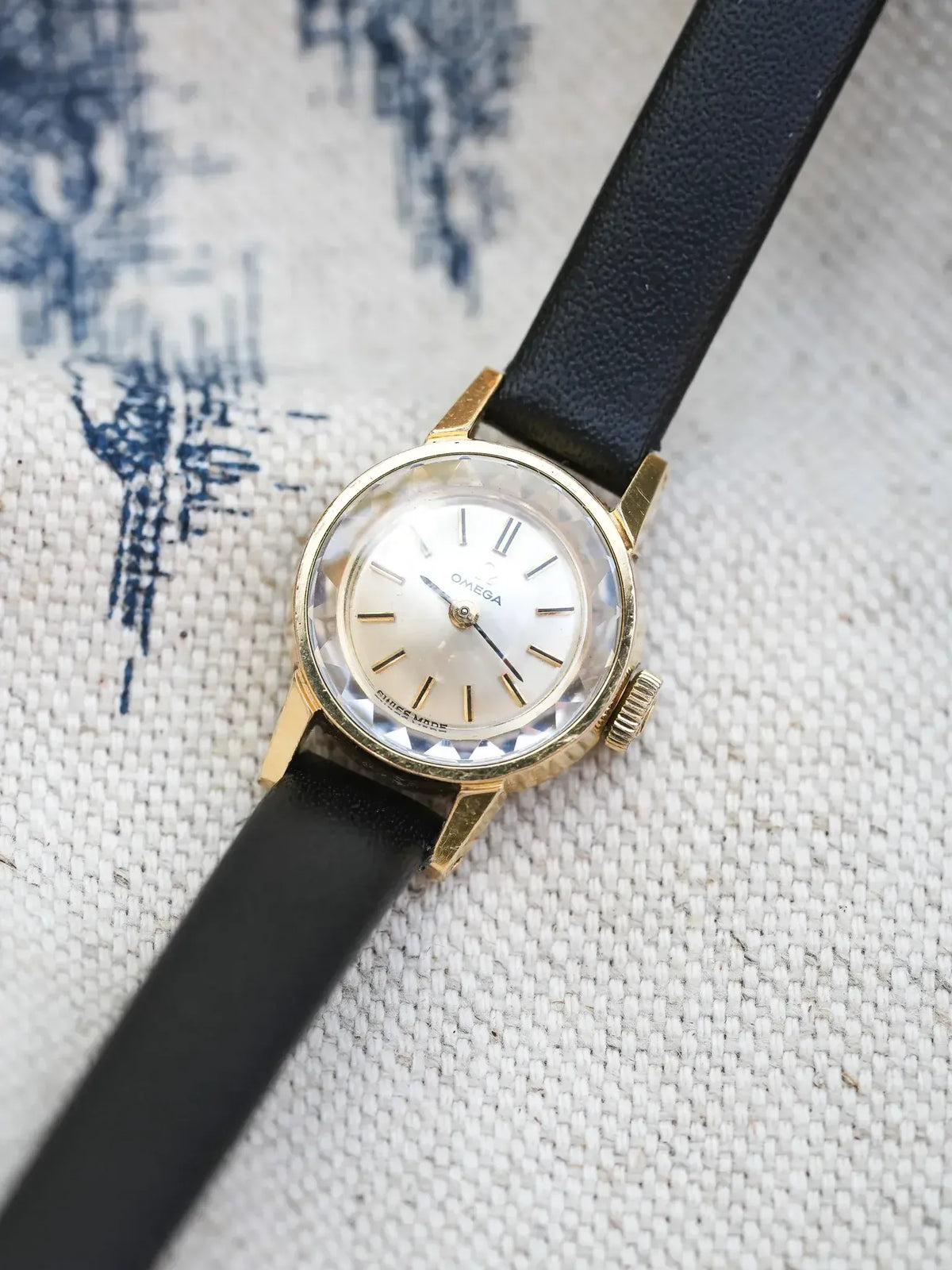 Vintage Omega watch with gold case, silver dial, black leather strap on fabric