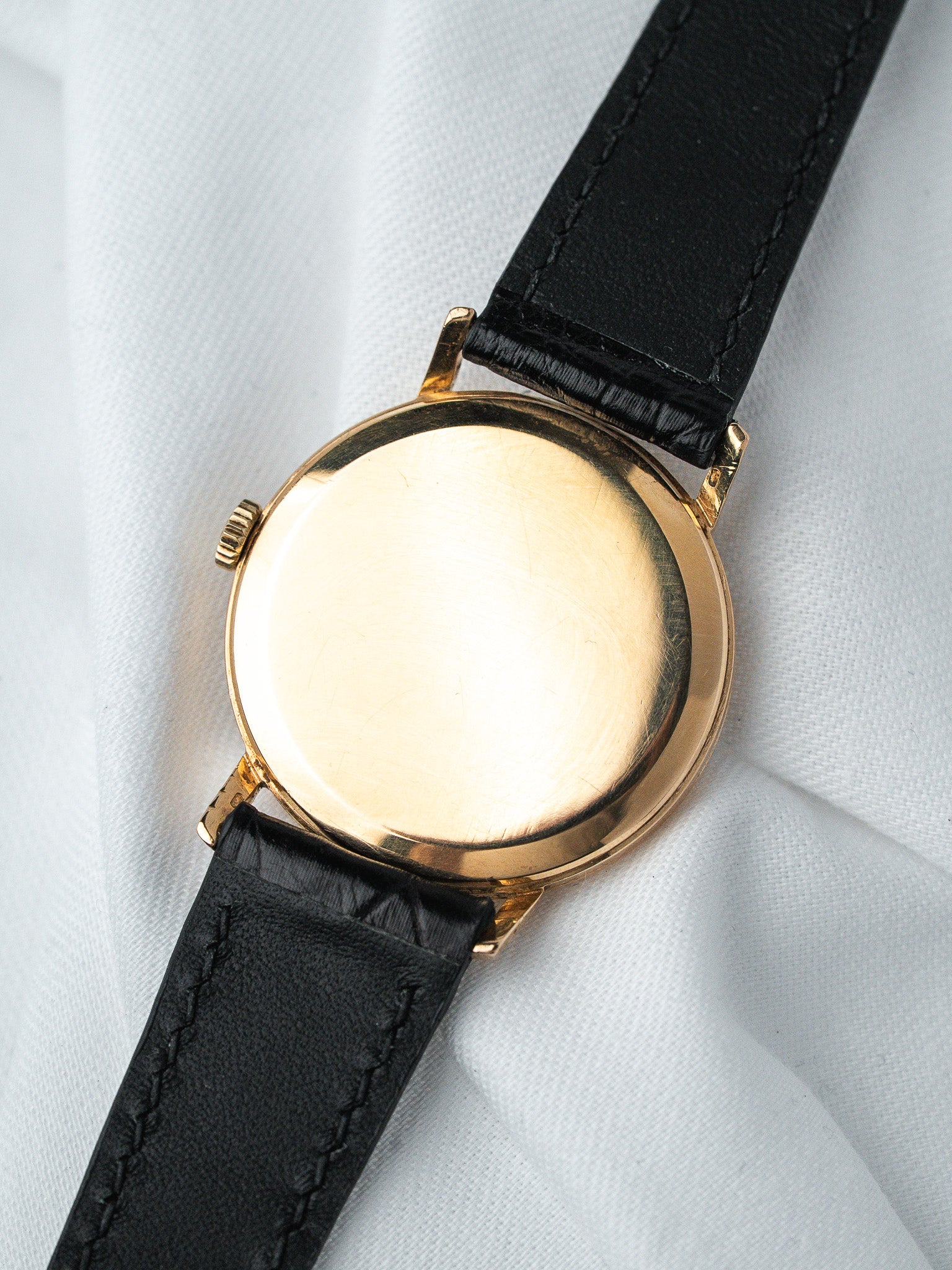Vintage gold watch case back with black leather strap on white fabric