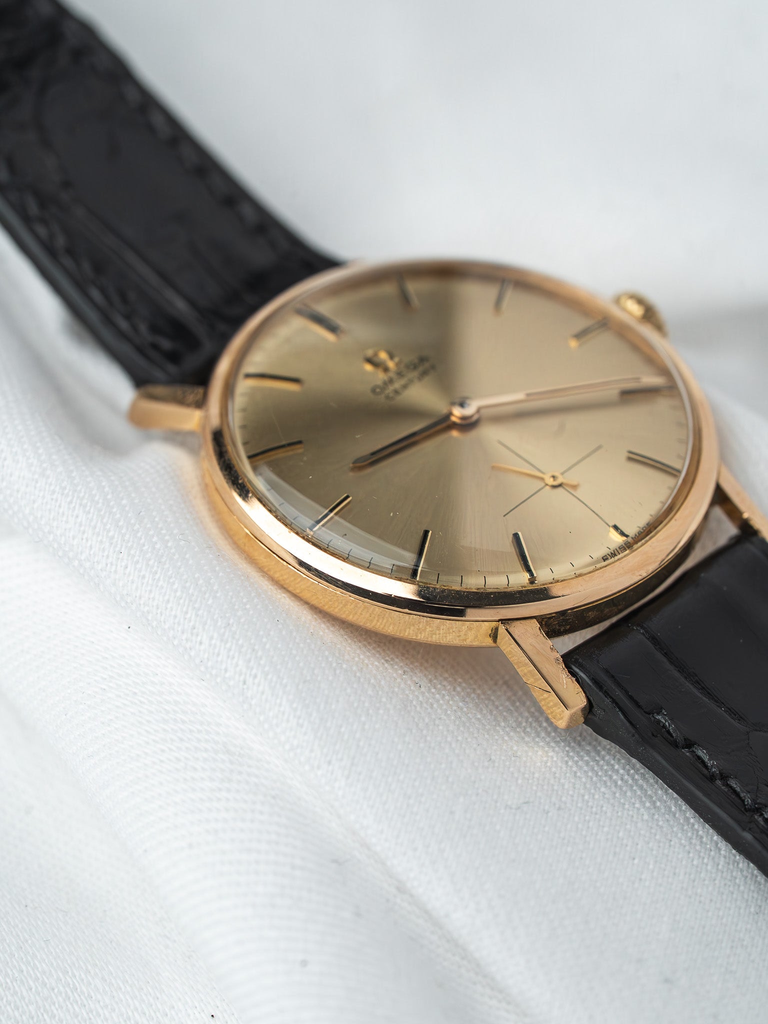 Omega vintage watch with gold case, champagne dial, and black leather strap