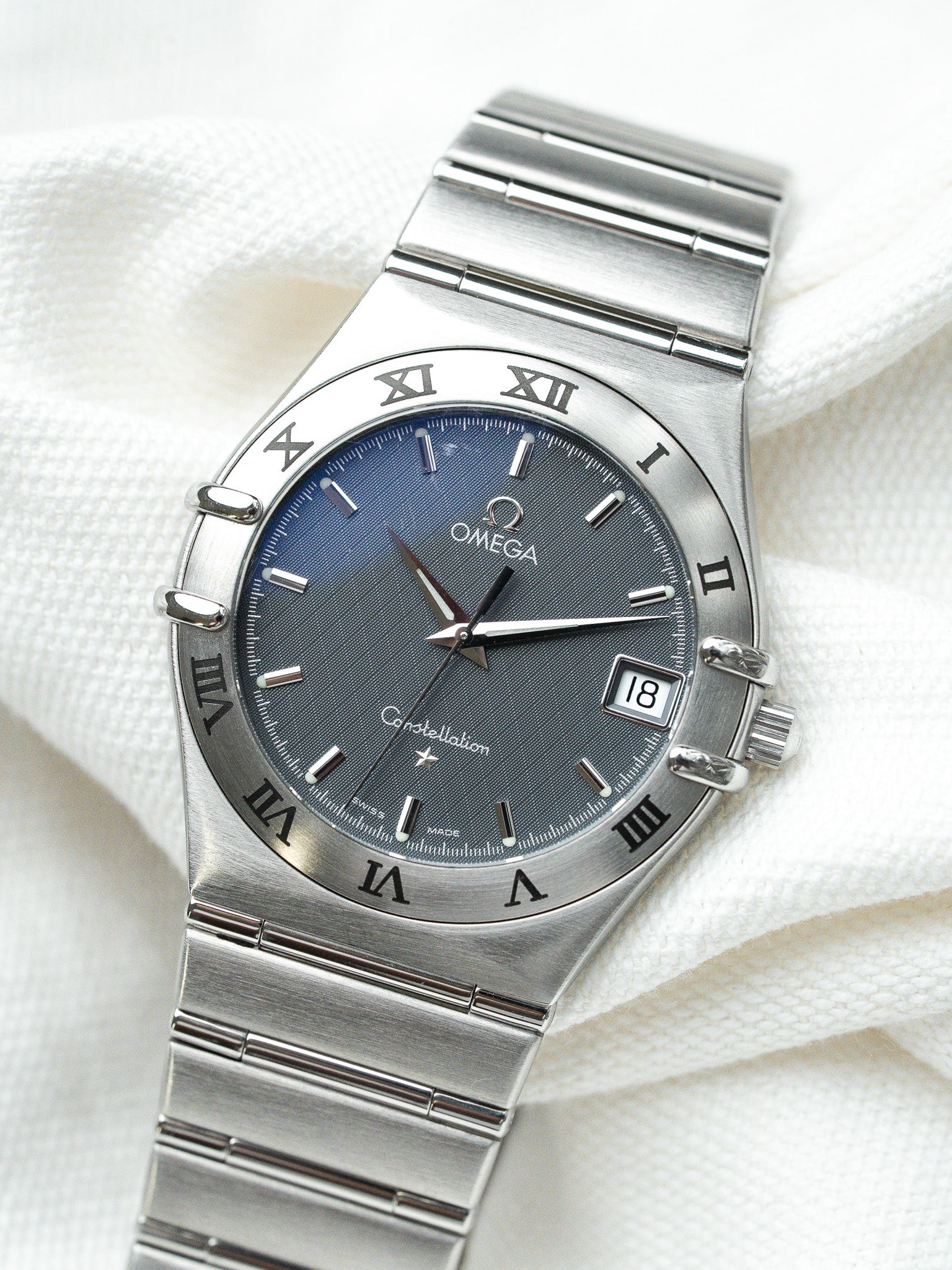 Omega Constellation watch with blue-grey dial, Roman numerals, steel bracelet on white fabric