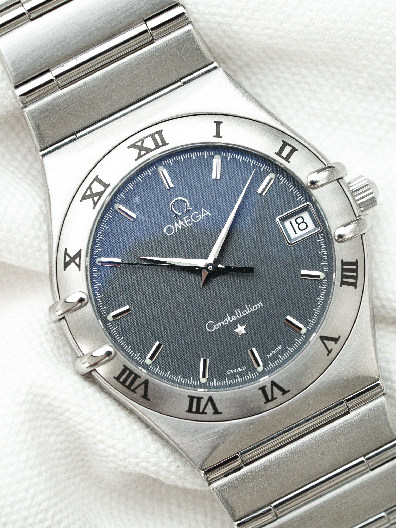 Omega Constellation watch with blue dial, Roman numerals, and steel bracelet on white fabric