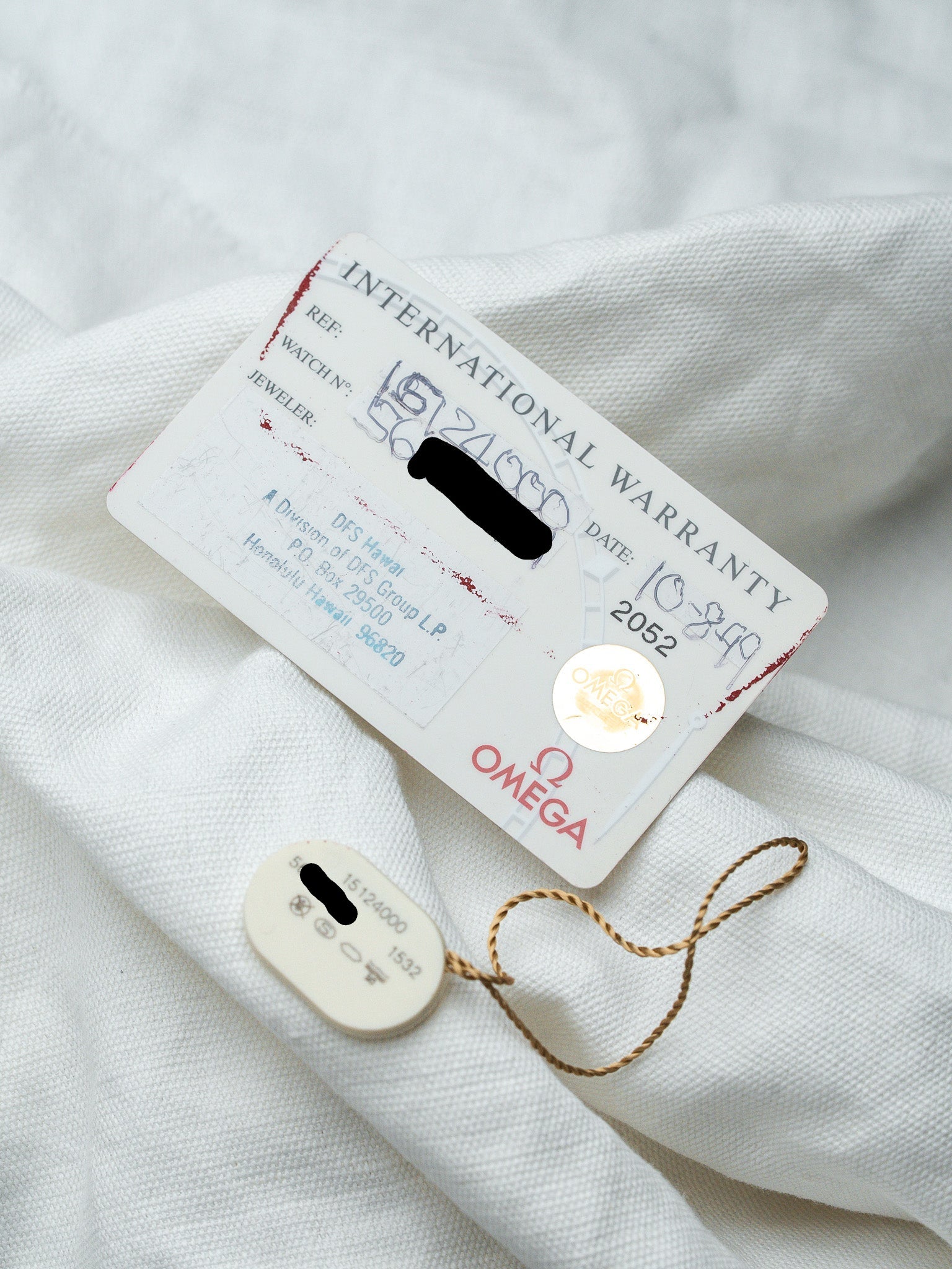 Omega International Warranty card with hologram seal and tag on white fabric