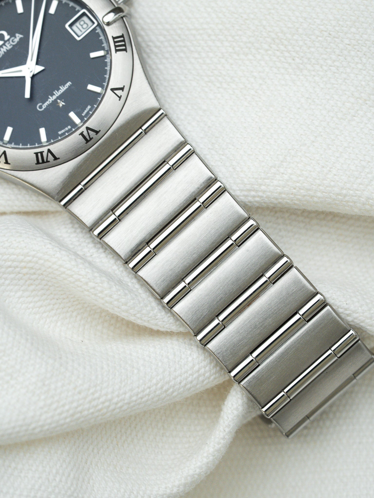 Omega Constellation vintage watch with dark dial, Roman numerals, and steel bracelet on white fabric