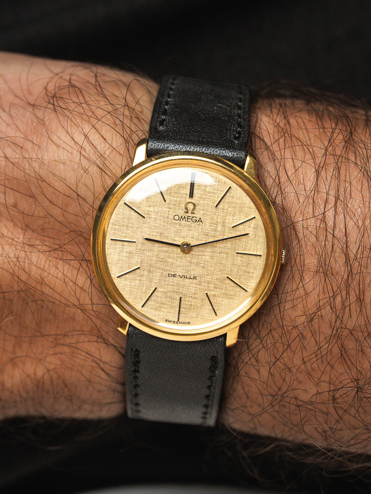 Montre Omega De Ville vintage en or, cadran doré et bracelet cuir noir au poignet