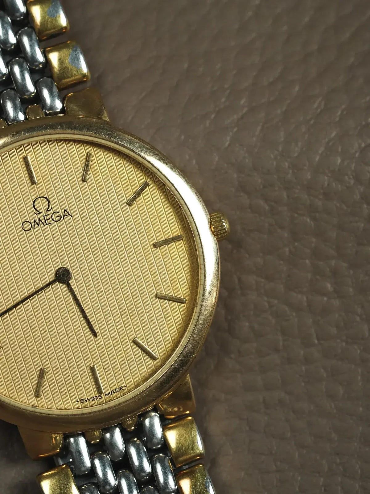 Omega vintage watch with gold dial, two-tone bracelet, on textured surface