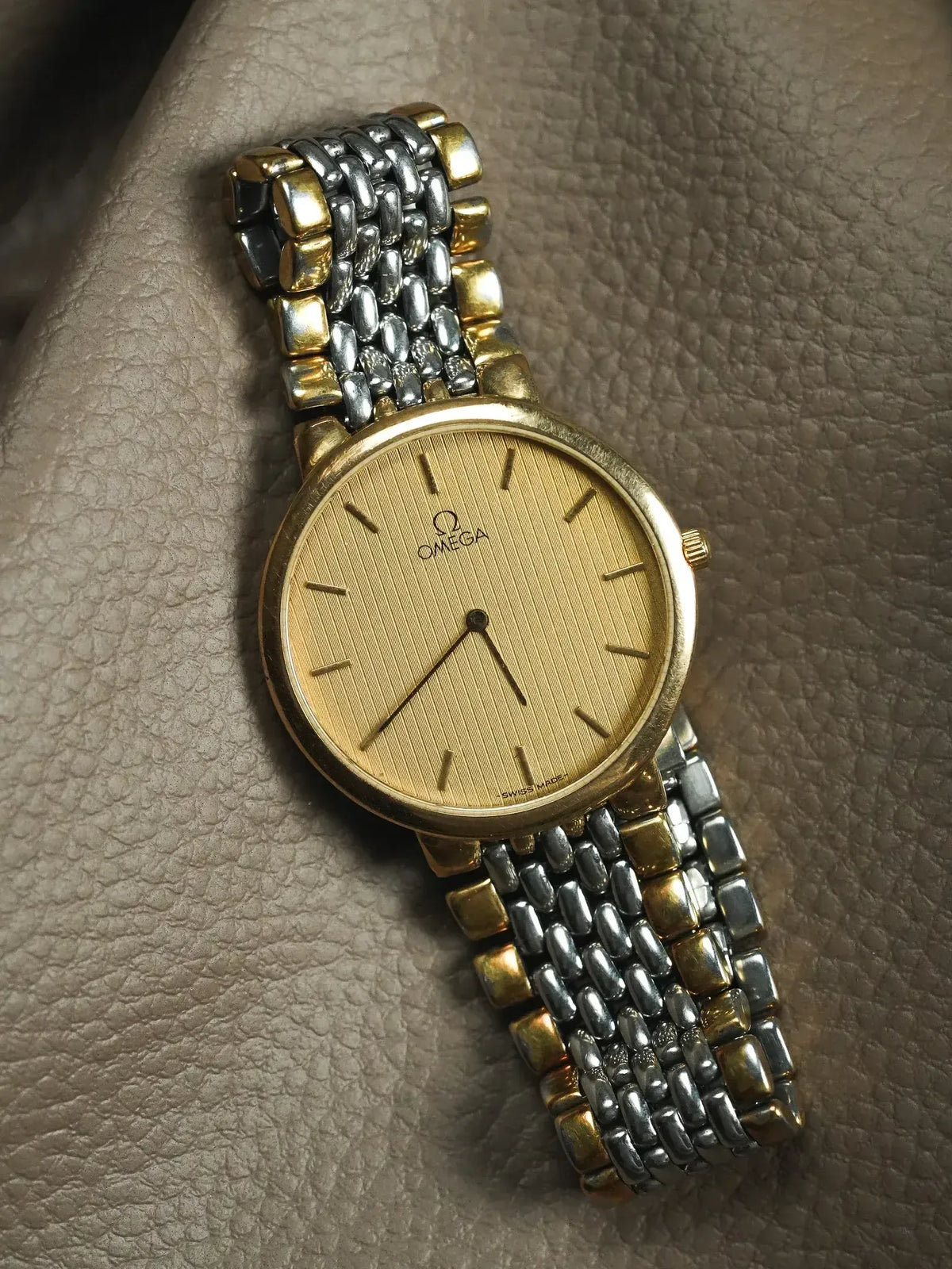 Omega vintage watch with gold dial and two-tone bracelet on textured leather