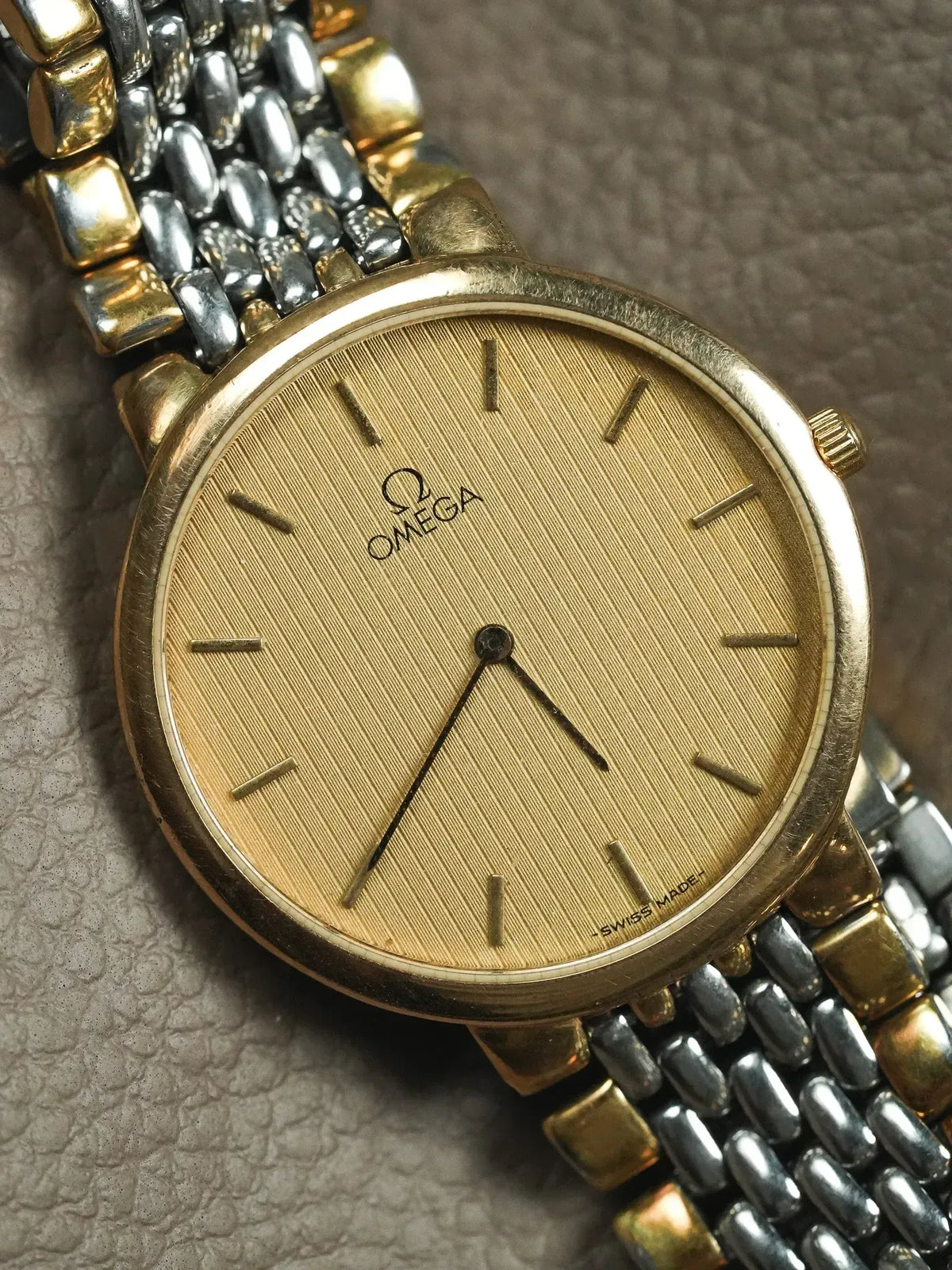 Omega vintage watch with gold dial, two-tone bracelet, on textured surface