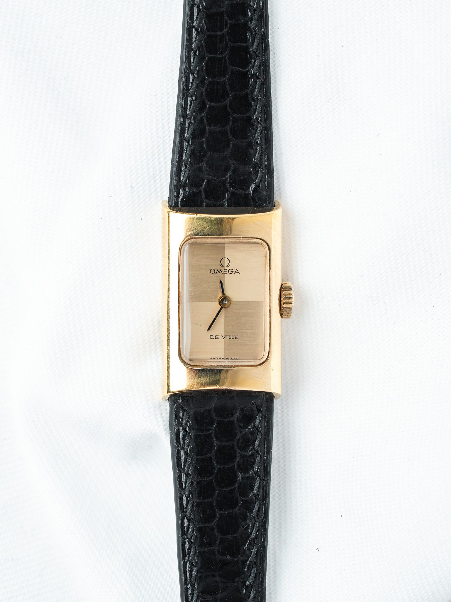 Omega De Ville vintage watch with gold case, beige dial, black alligator strap on white background