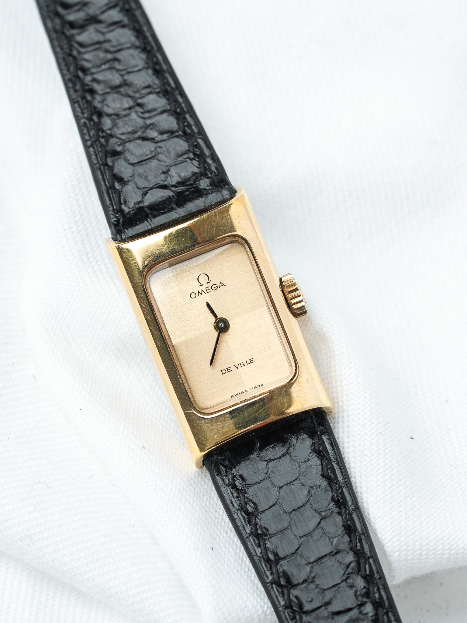 Omega De Ville vintage watch with gold case, cream dial, black alligator strap on white background