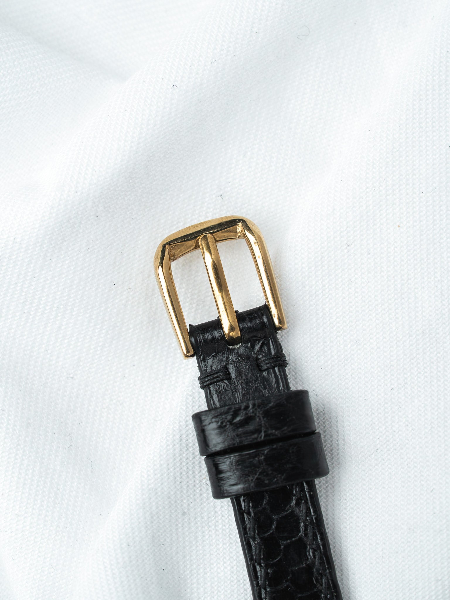 Black alligator leather watch strap with gold buckle on white background