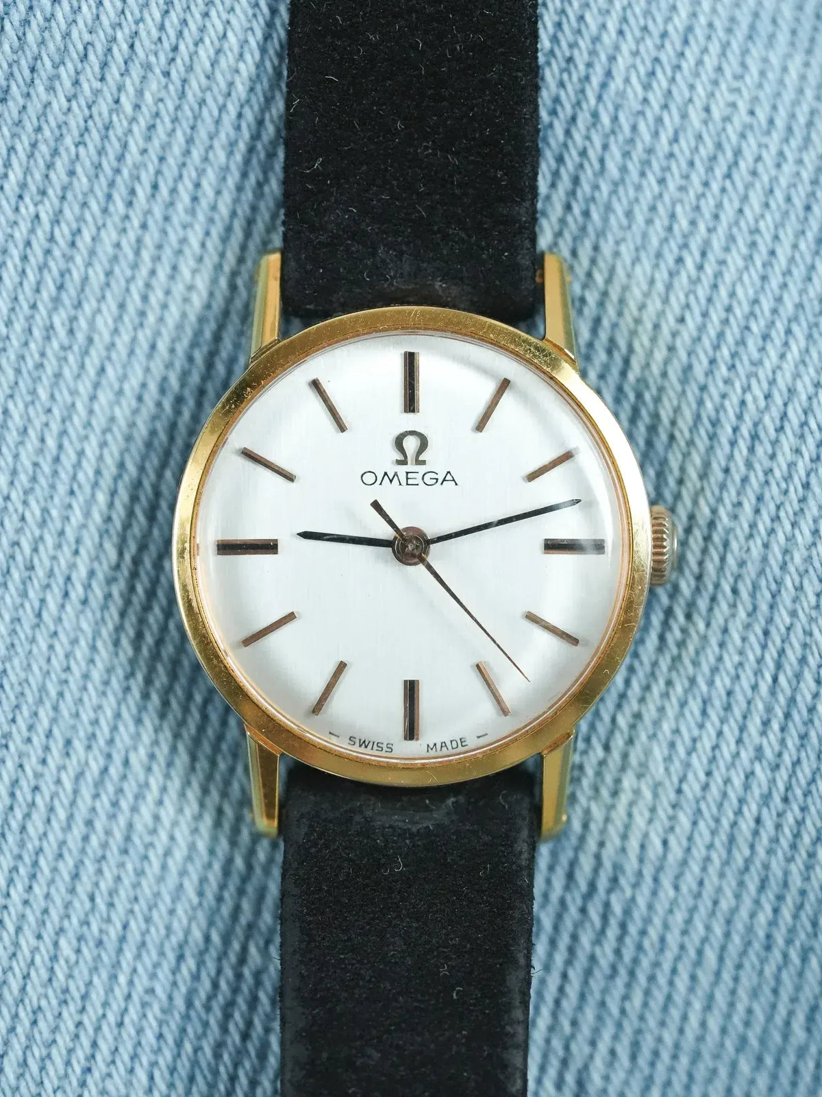 Omega vintage watch with gold case, white dial, black strap on denim