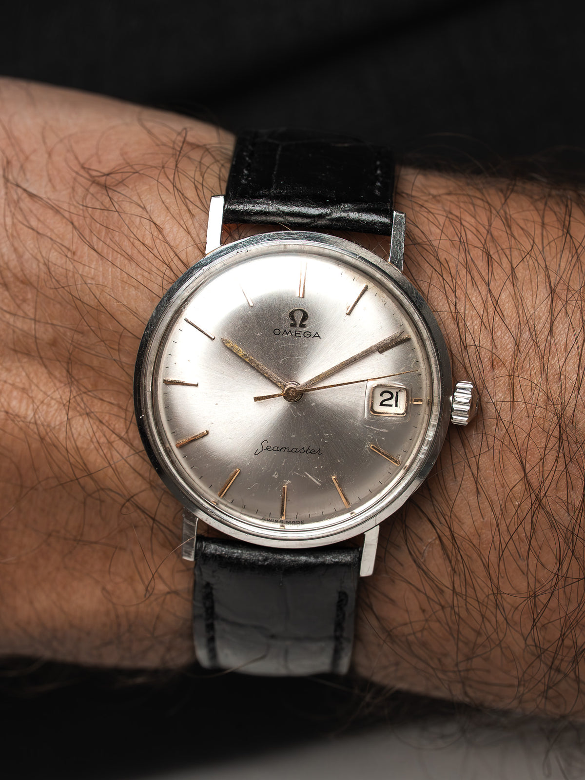 Montre Omega Seamaster vintage, cadran argenté et bracelet cuir noir, portée au poignet