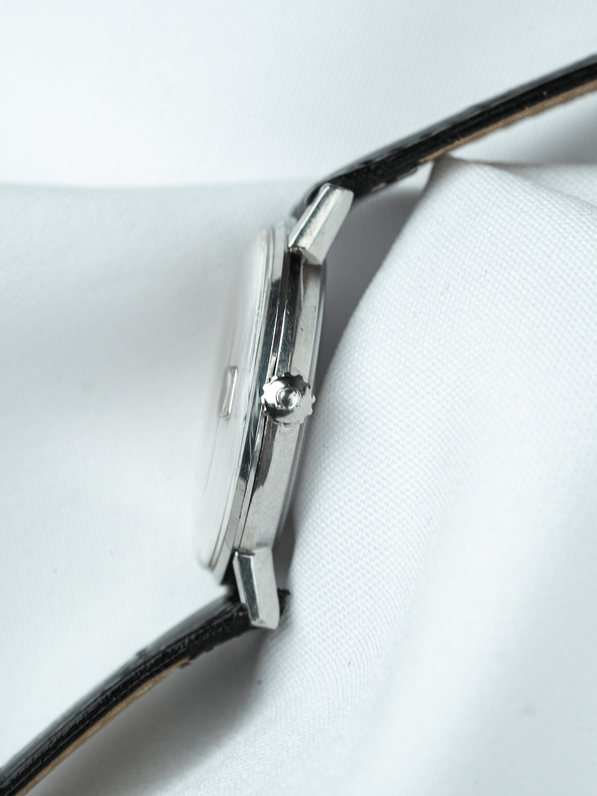 Vintage watch with black leather strap and silver case on white fabric