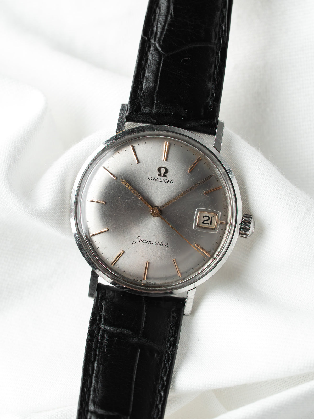 Montre Omega Seamaster vintage, cadran argenté et bracelet en cuir noir sur fond blanc