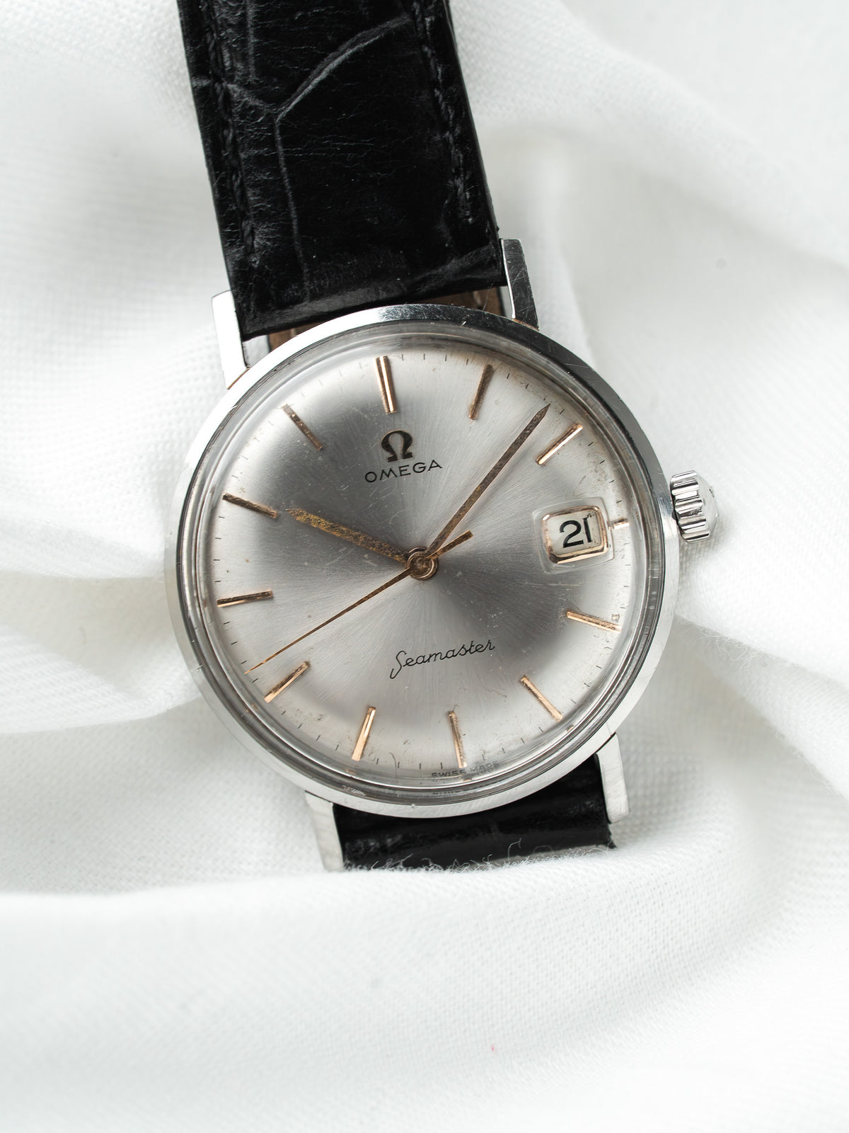 Montre Omega Seamaster vintage, cadran argenté et bracelet en cuir noir sur fond blanc